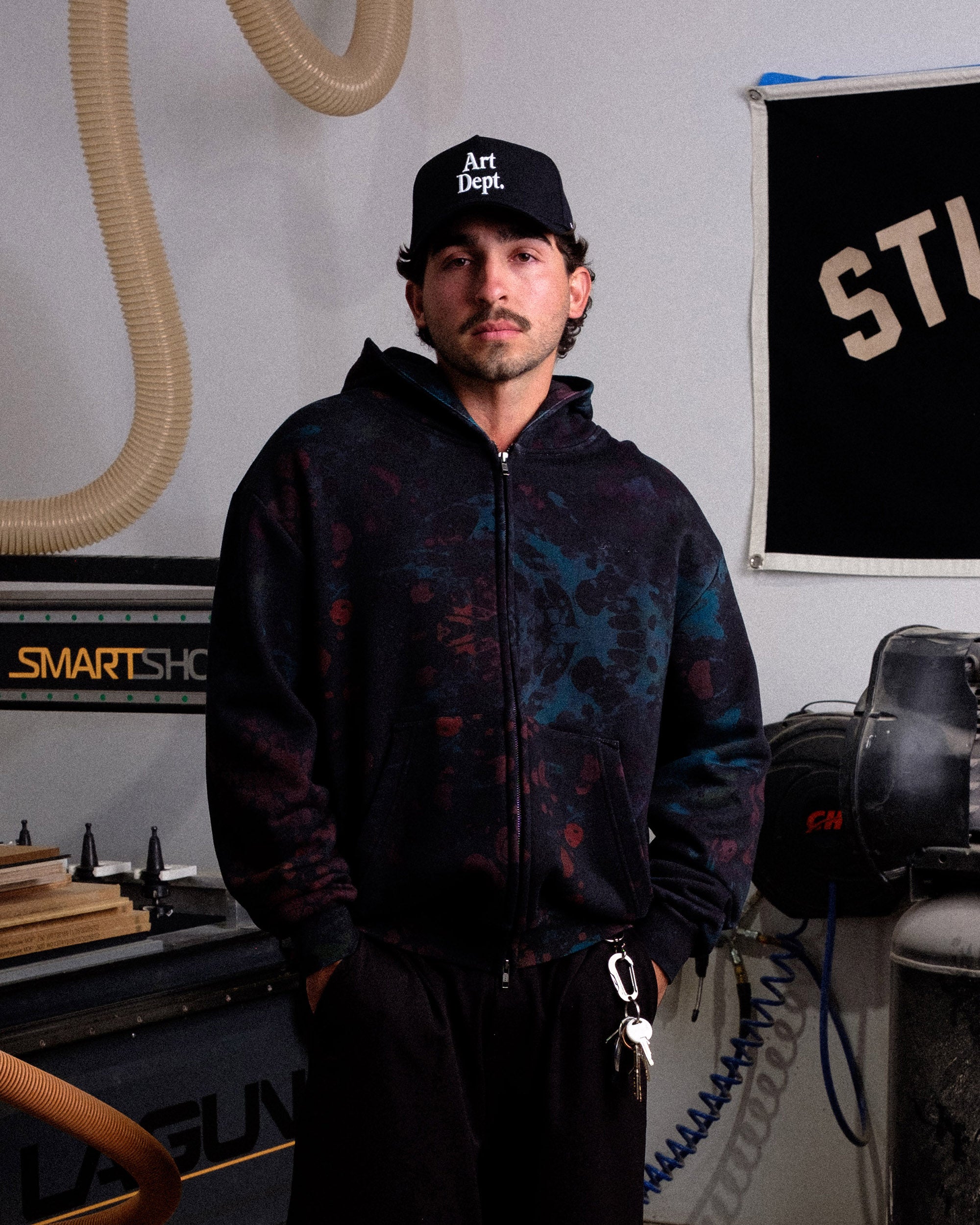 Man wearing a black hoodie and cap in a workshop setting