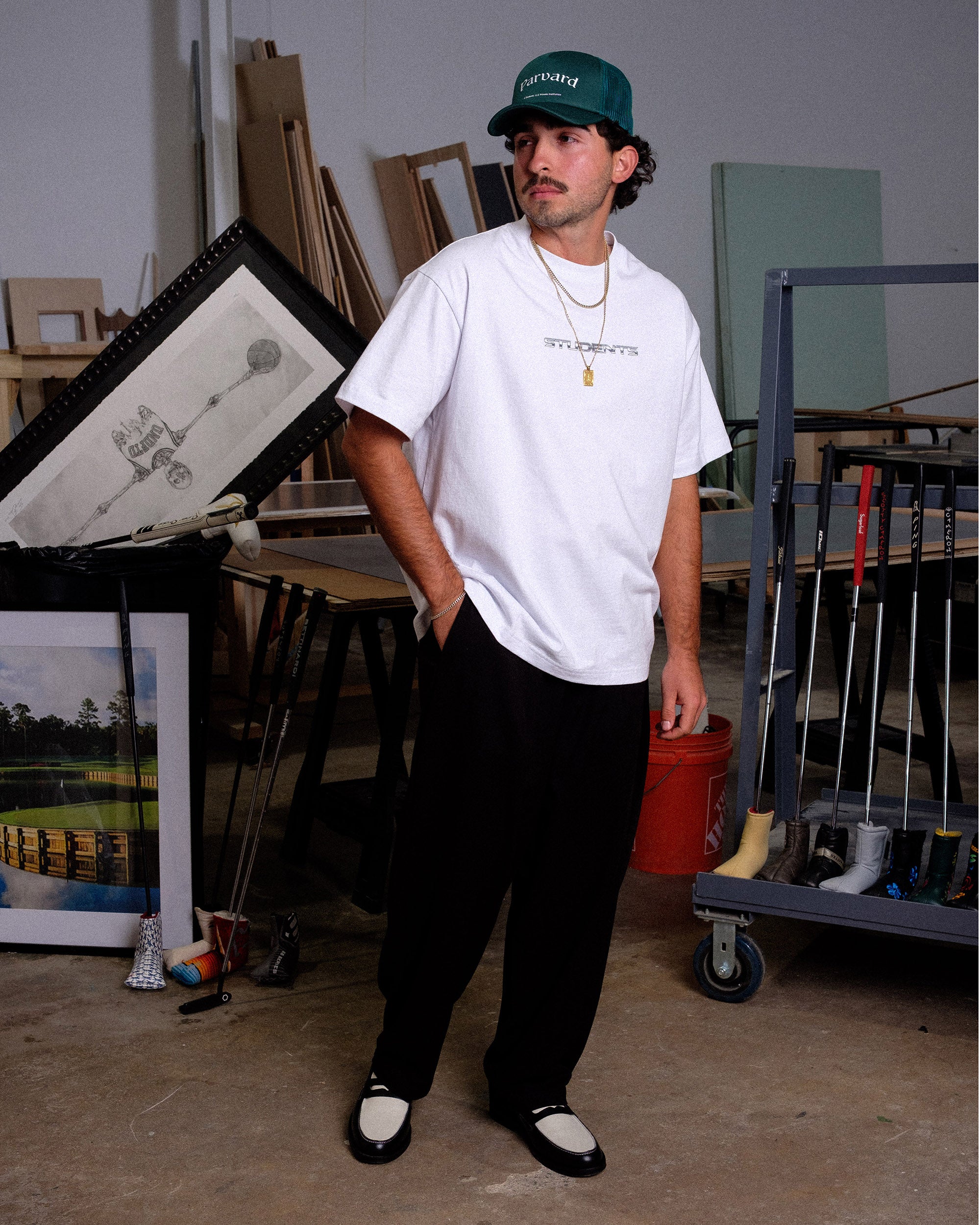 Man wearing a white t-shirt and black pants standing in an art studio.