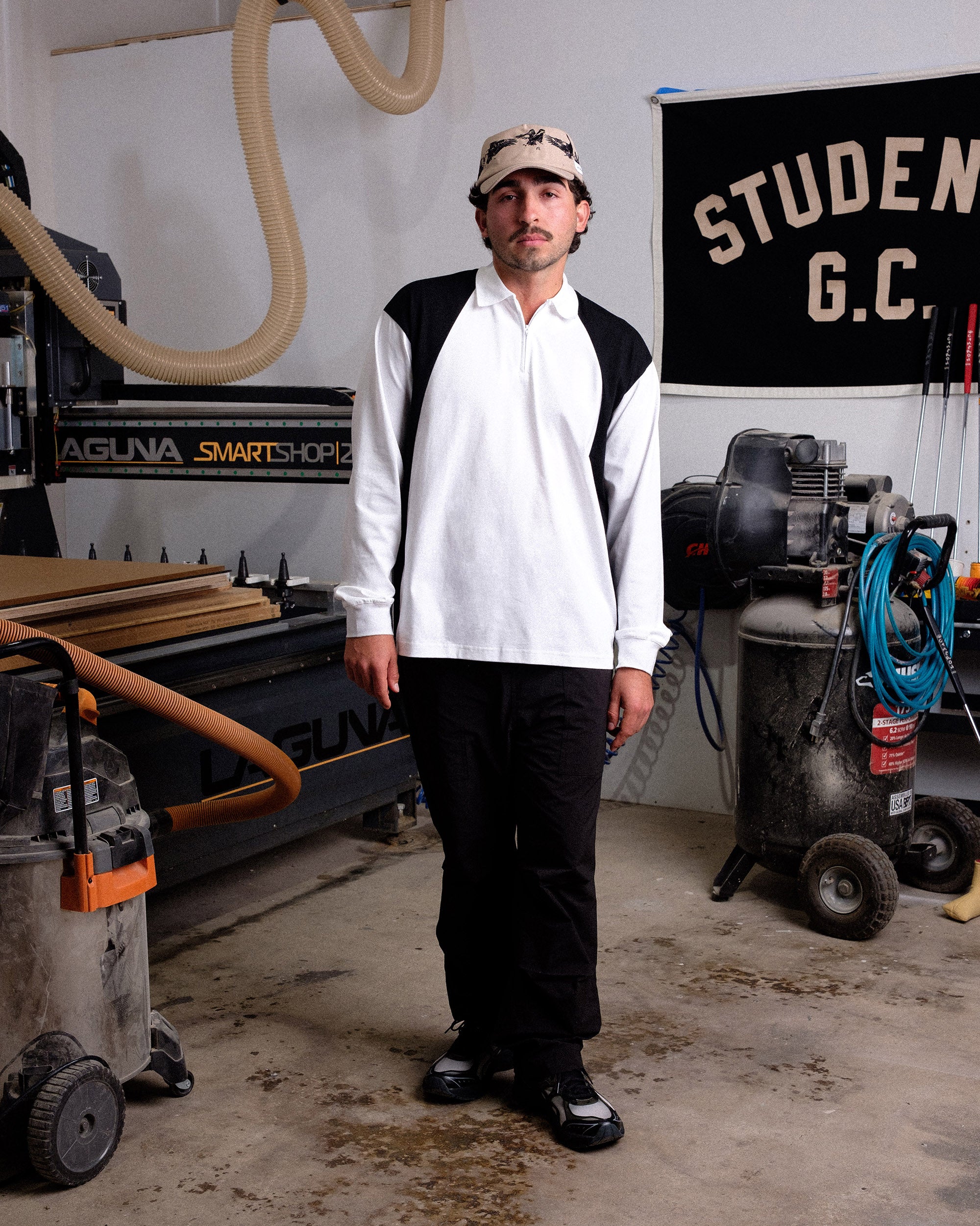 Man standing in a workshop with industrial equipment and a 'STUDENTS G.C.' banner in the background.