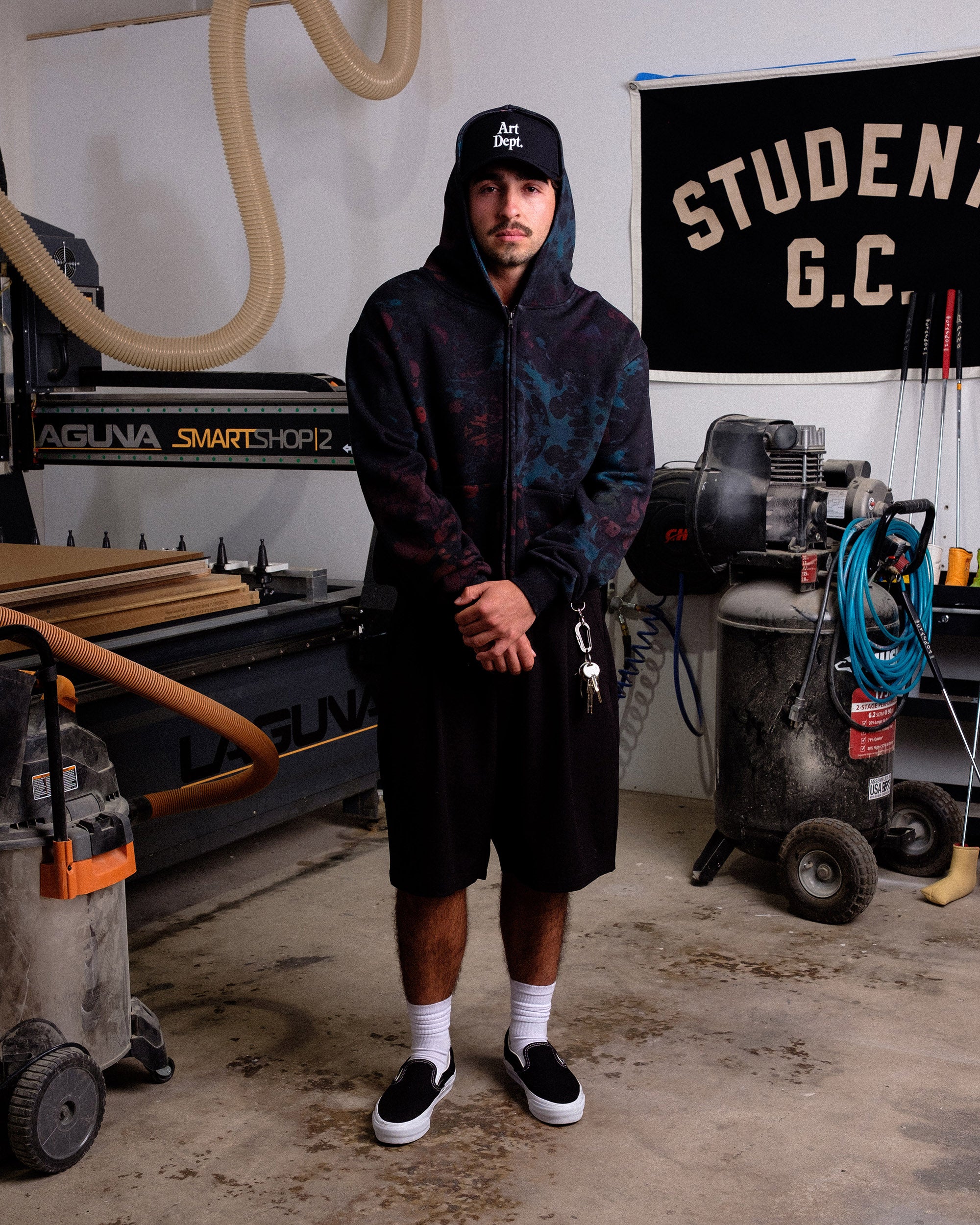 Person wearing a dark hoodie and shorts in a workshop setting
