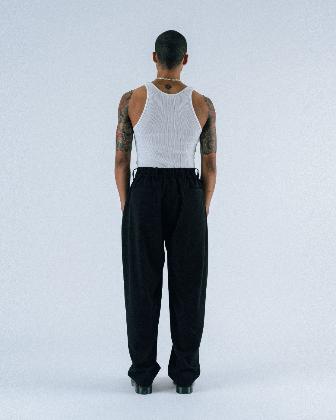 Person wearing a white tank top and black pants on a light gray background