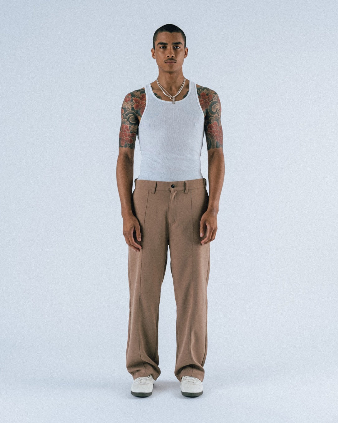 Man wearing a white tank top and beige pants on a light gray background