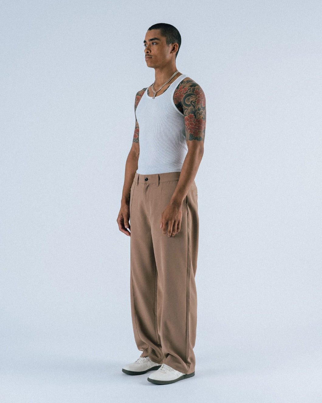 Man wearing a white tank top and brown pants on a white background