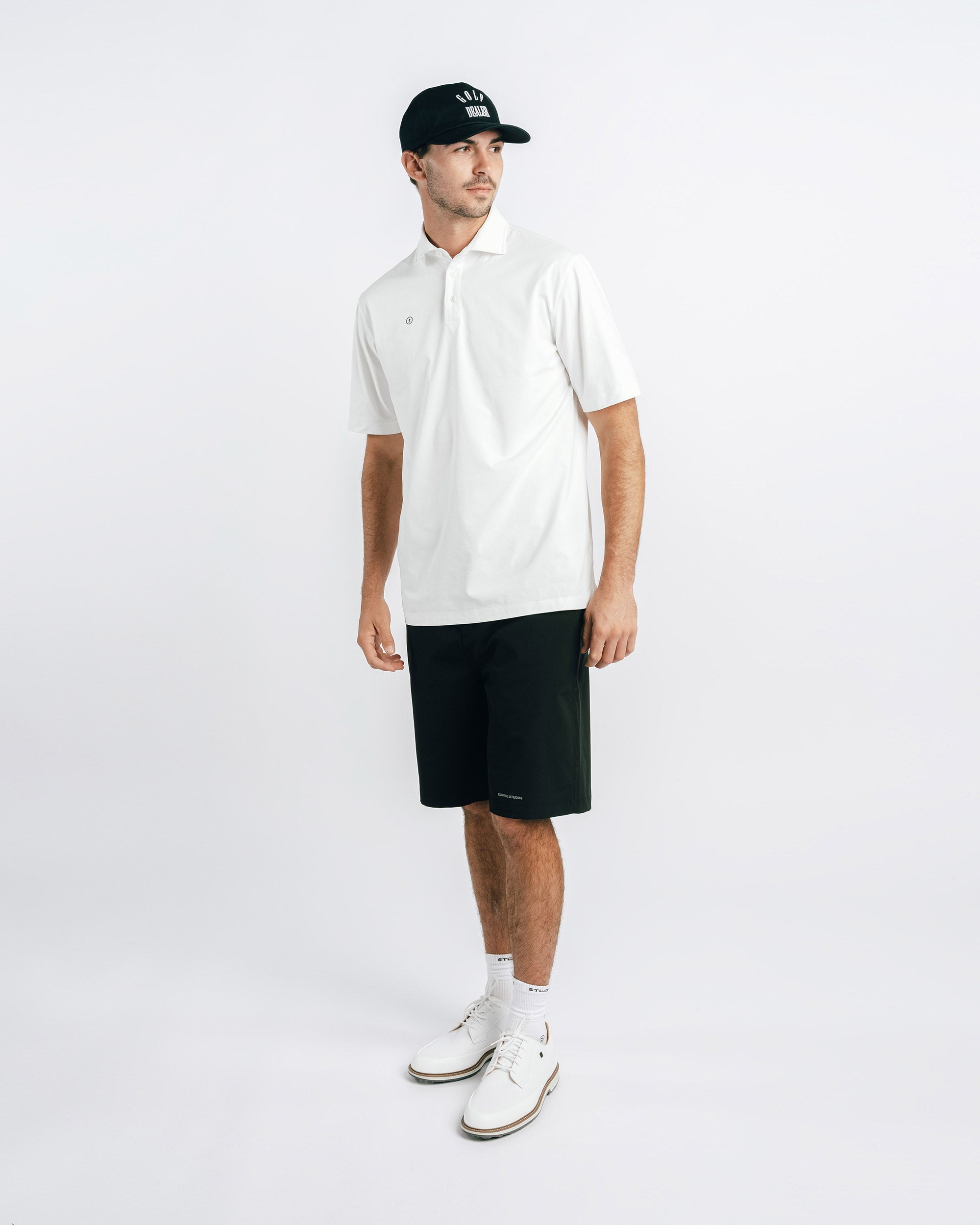 Man wearing a white polo shirt, black shorts, and a black cap on a white background