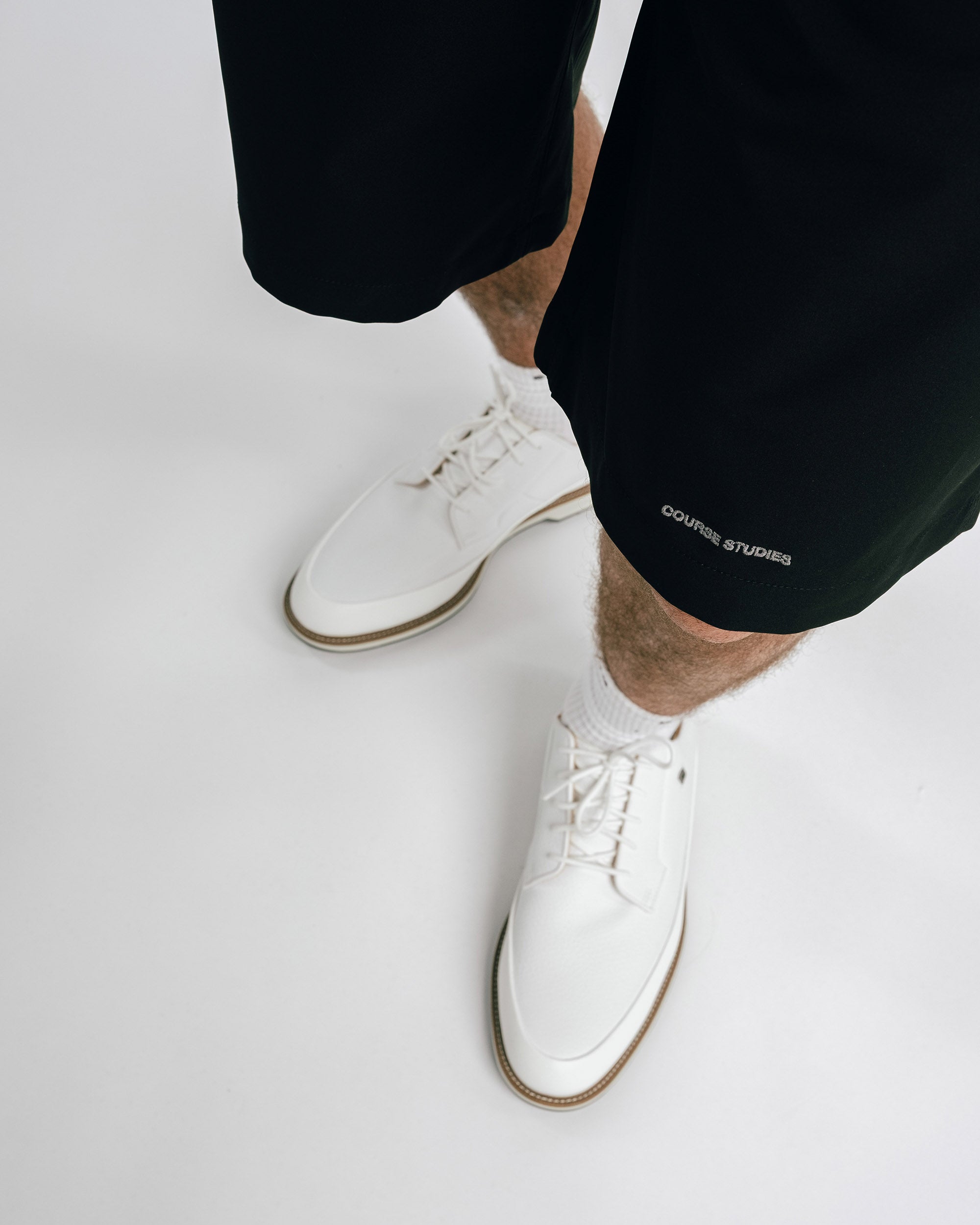 Person wearing black shorts with 'Golf le Fleur' branding and white sneakers on a light gray background