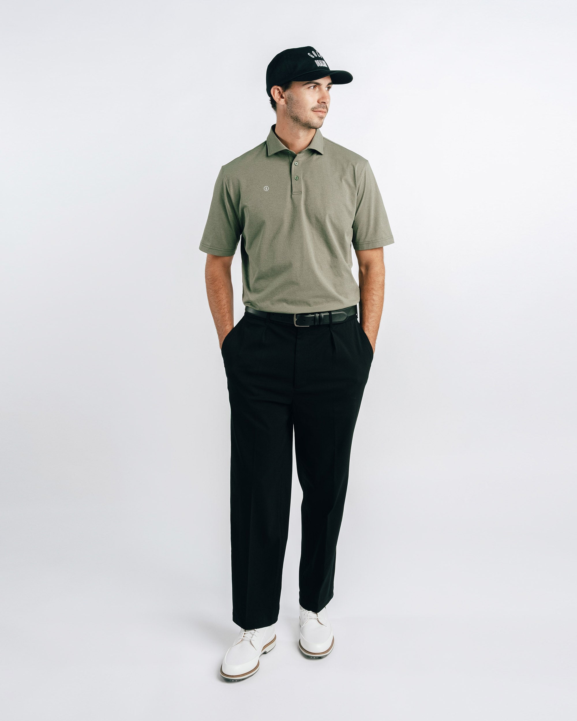 Man wearing a green polo shirt, black pants, and white shoes on a white background
