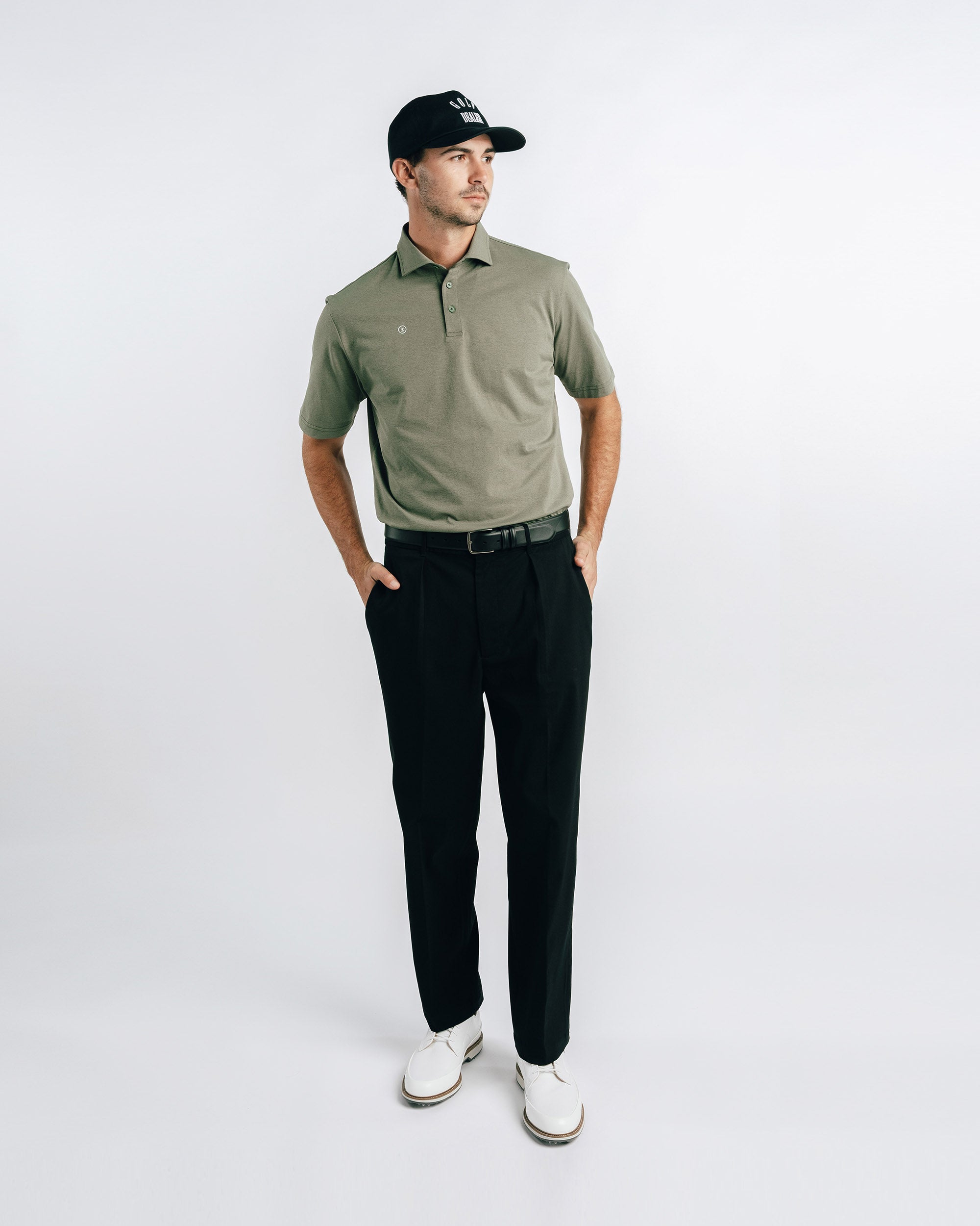 Man wearing a green polo shirt, black pants, and a black cap on a white background