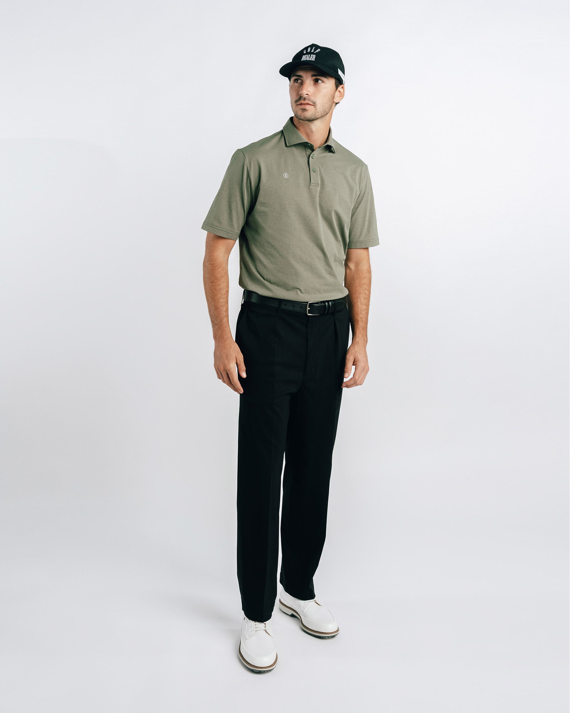 Man wearing a green polo shirt, black pants, and white shoes on a white background