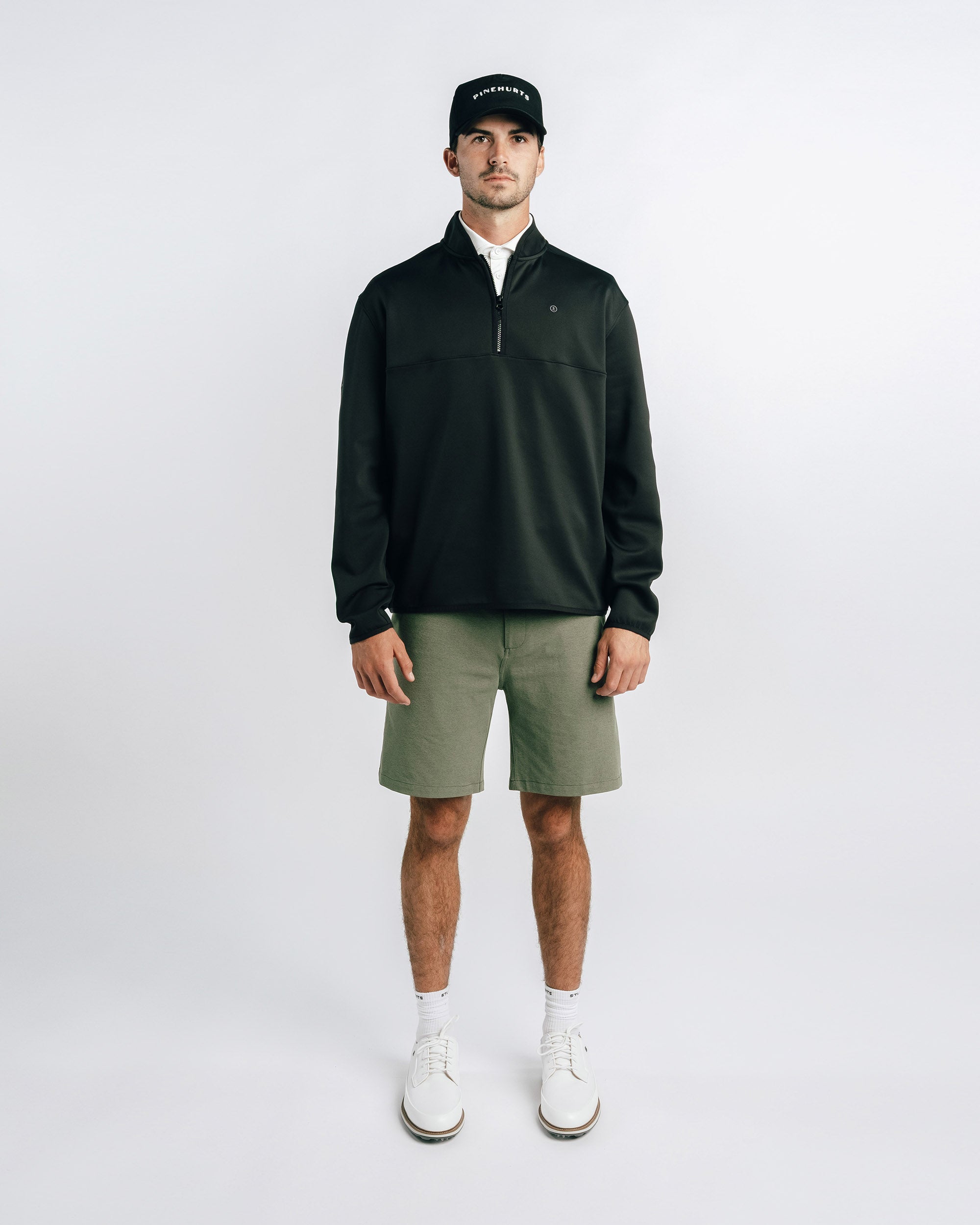 Man wearing a black jacket, green shorts, and white shoes on a white background