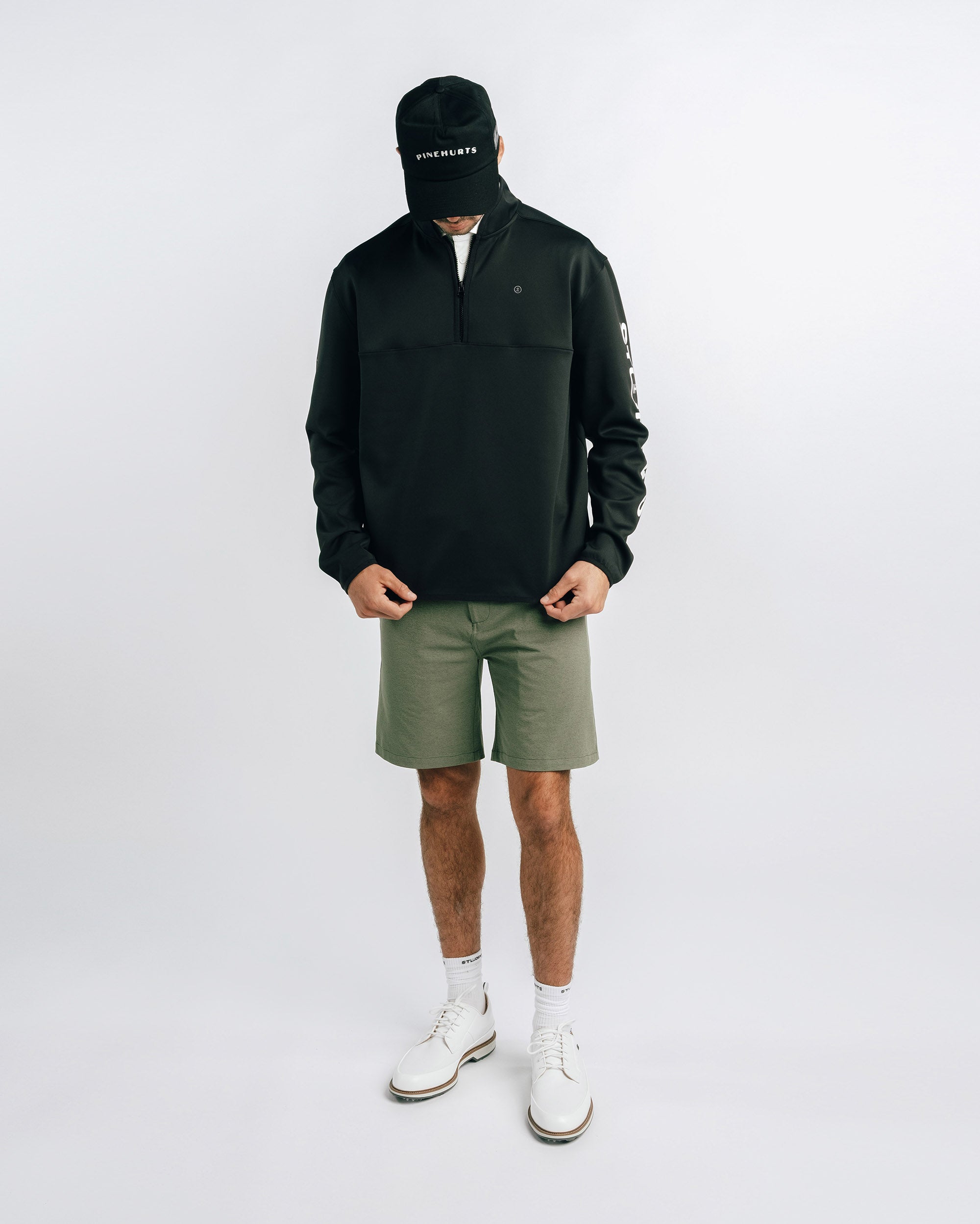 Person wearing a black jacket, green shorts, and white shoes on a white background