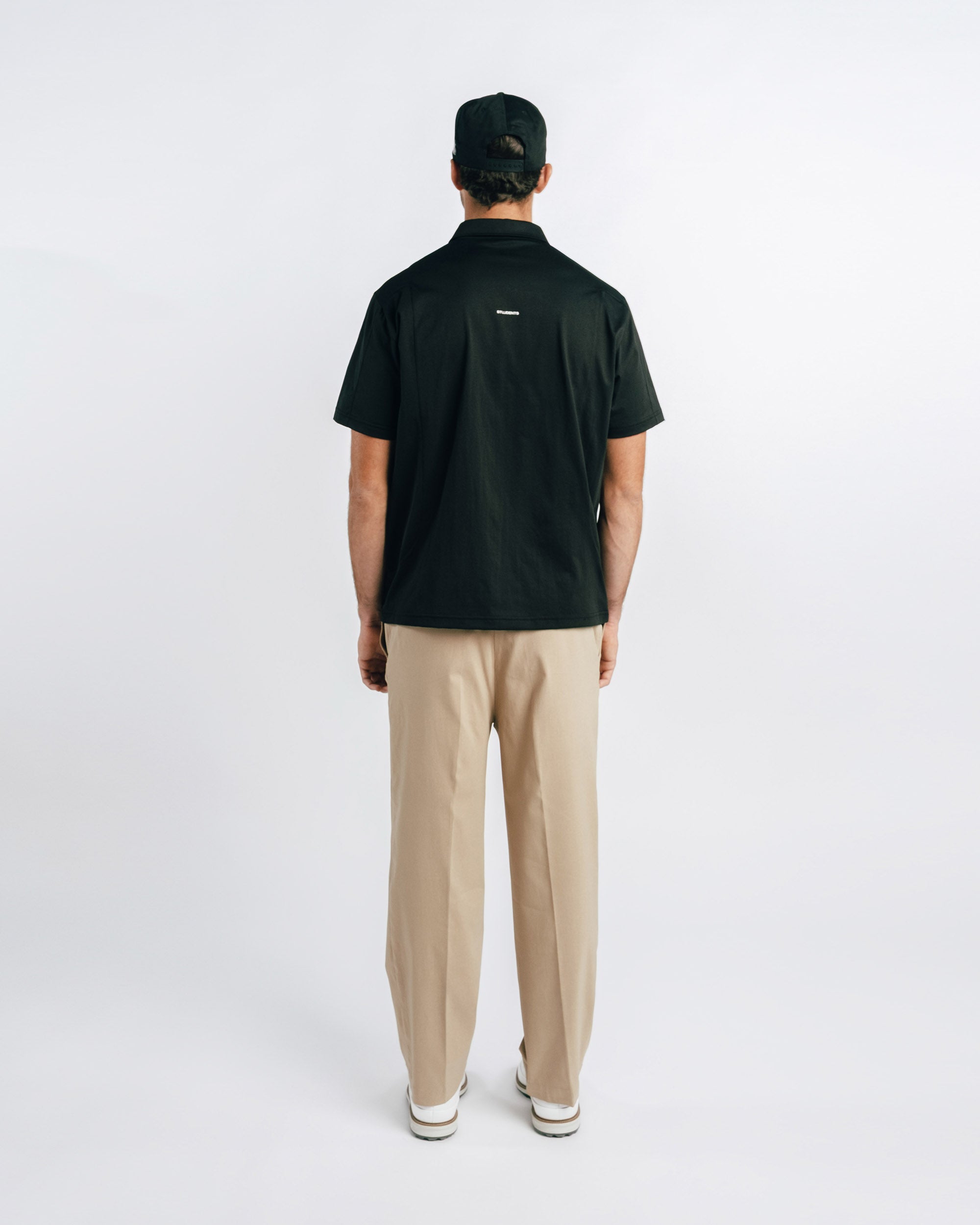 Person wearing a black polo shirt and beige pants on a white background