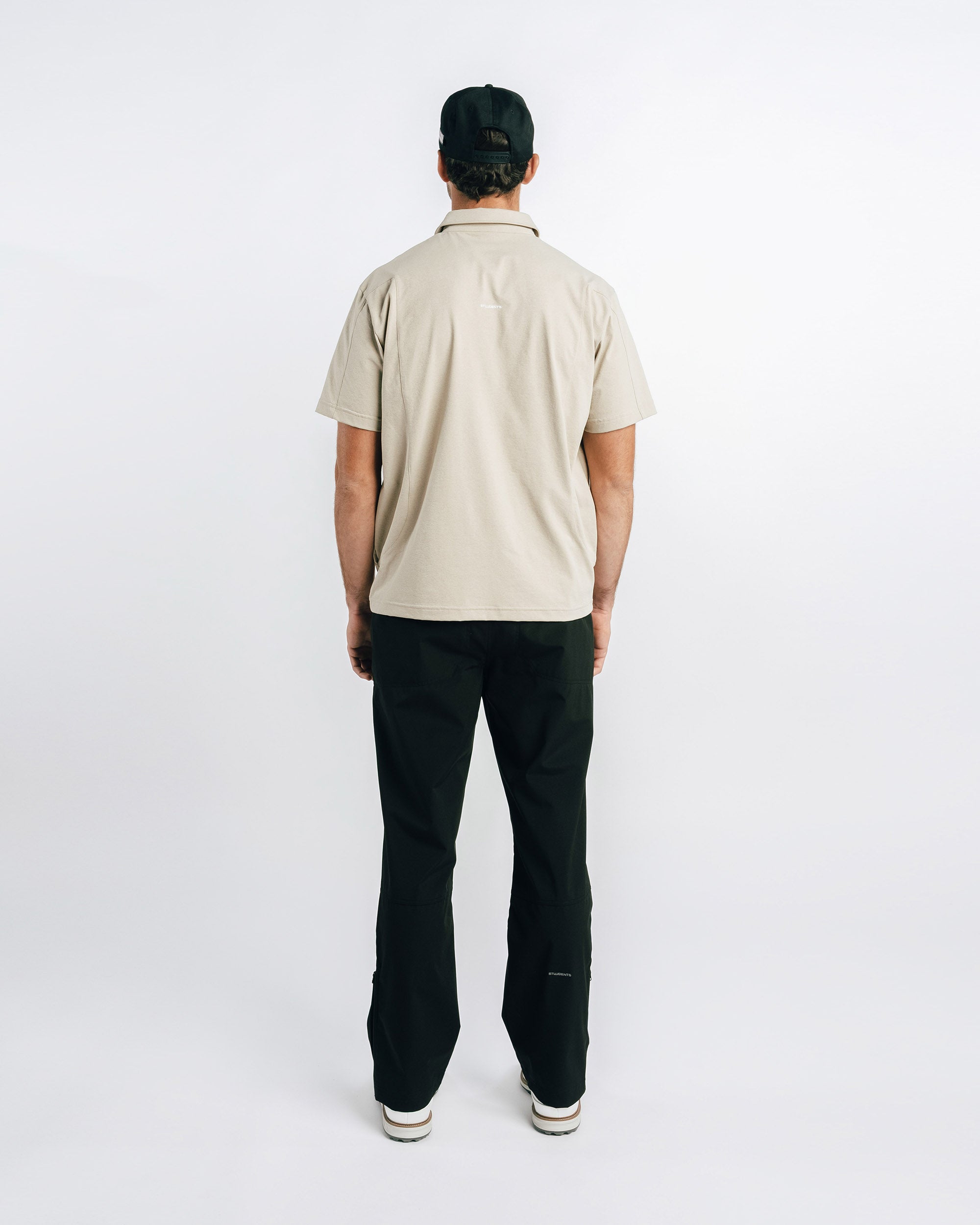 Person wearing a beige polo shirt and black pants on a white background
