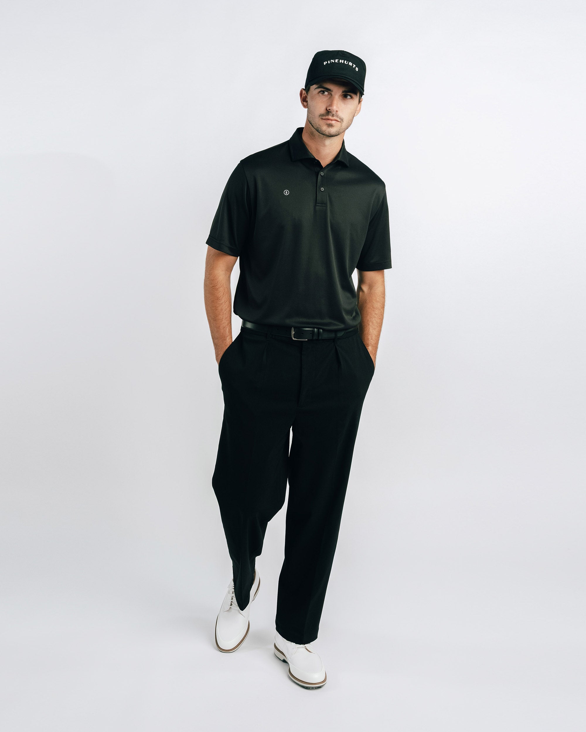 Man wearing a black polo shirt, black pants, and white shoes on a white background
