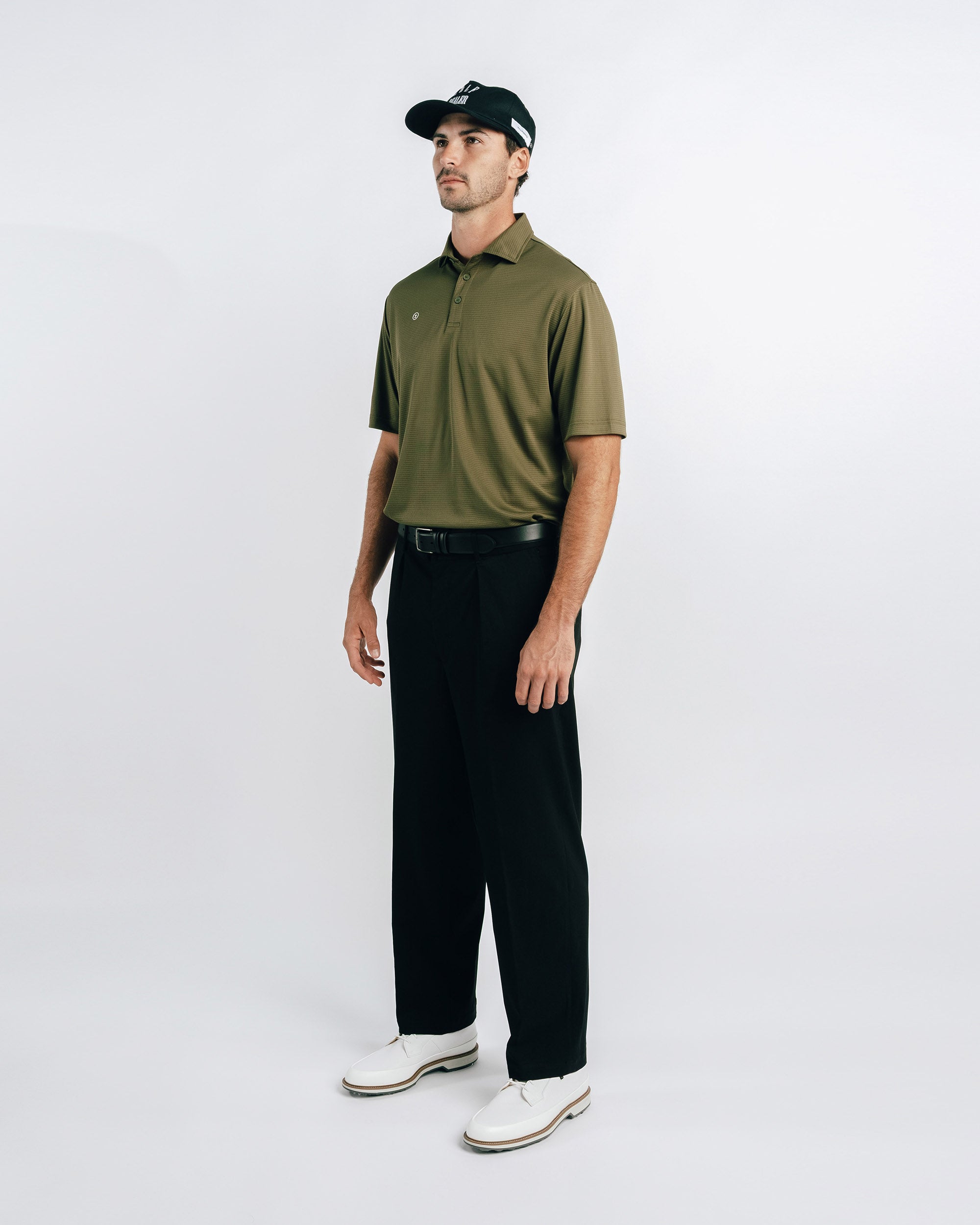 Man wearing an olive green polo shirt, black pants, and a cap on a white background
