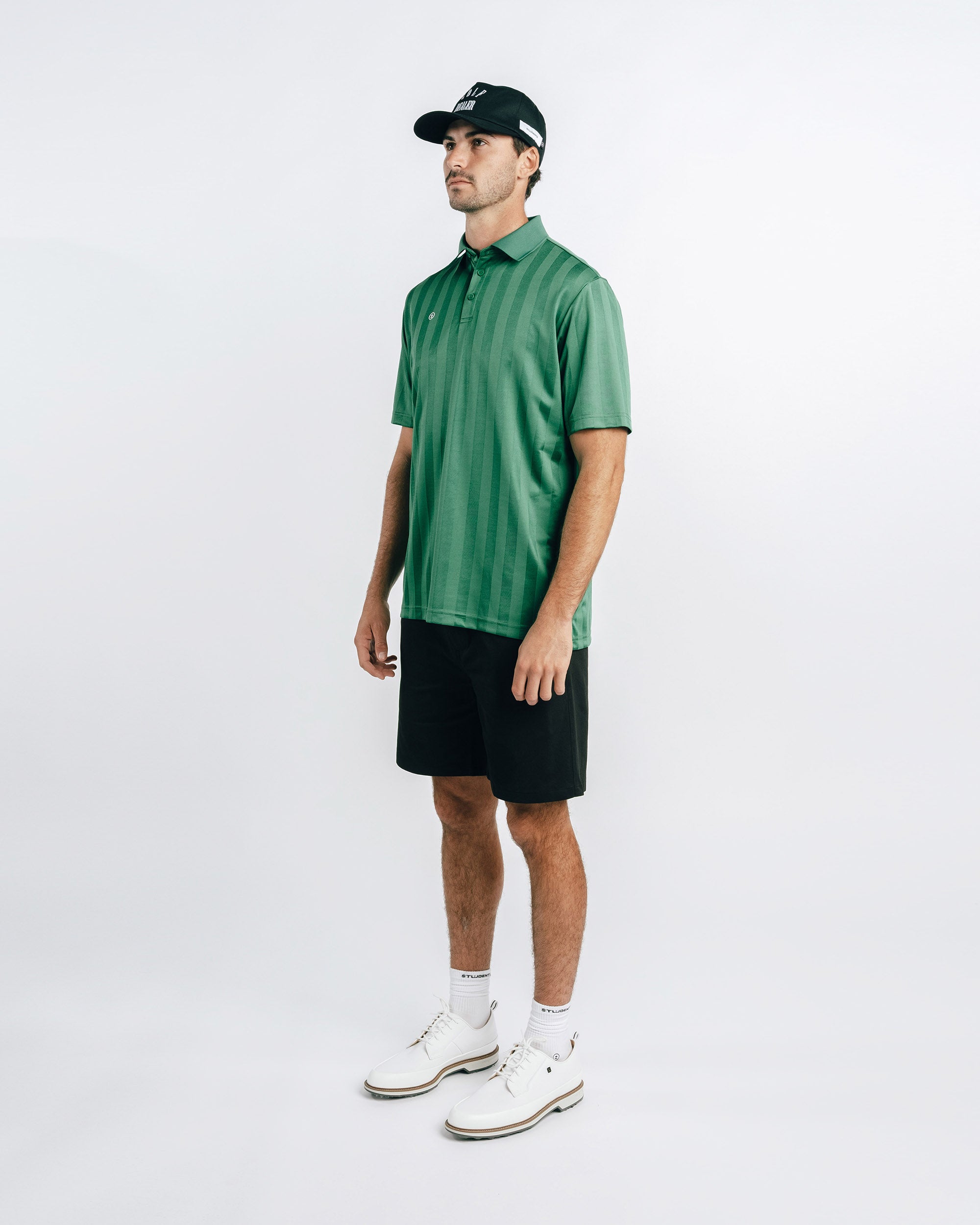Man wearing a green polo shirt, black shorts, and white shoes on a white background