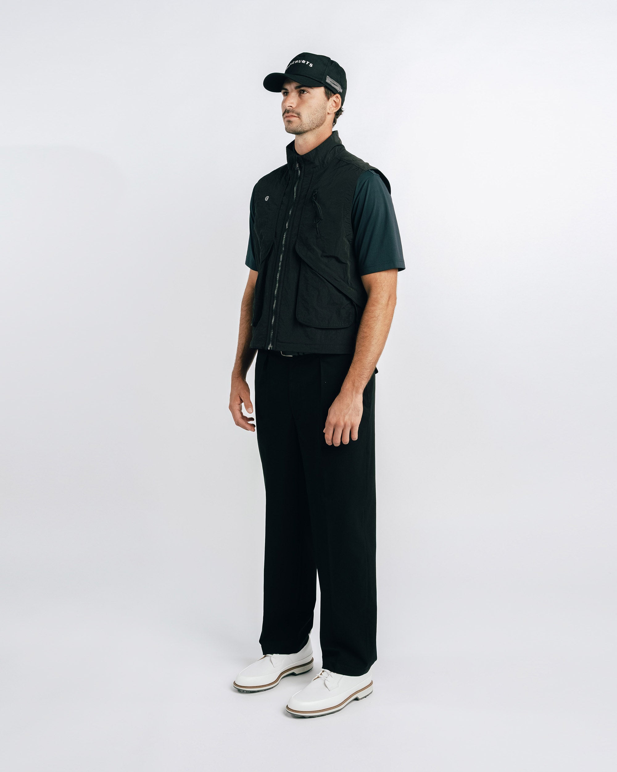 Man wearing a black outfit with a vest and cap on a white background