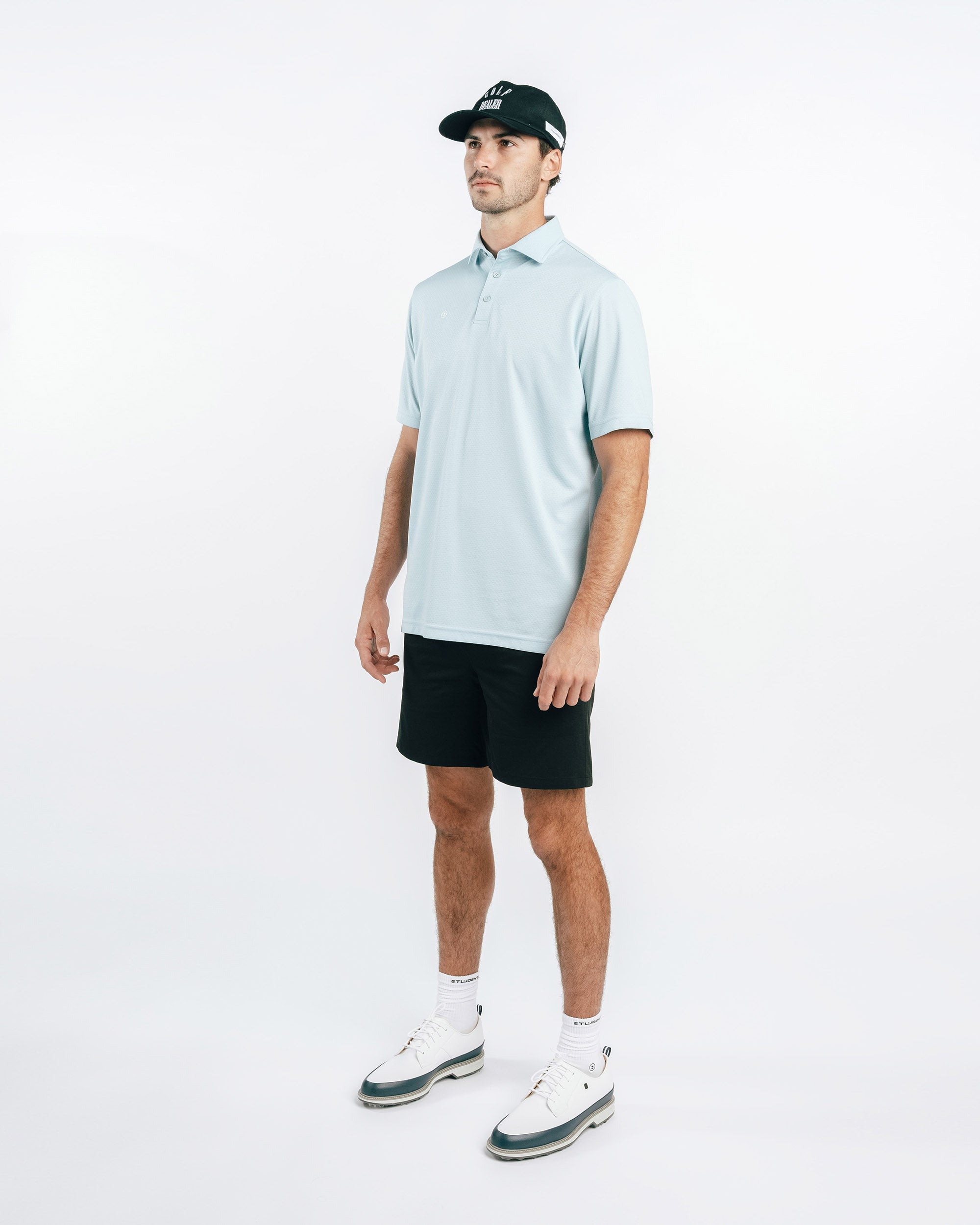 Man wearing a light blue polo shirt, black shorts, and white sneakers on a white background