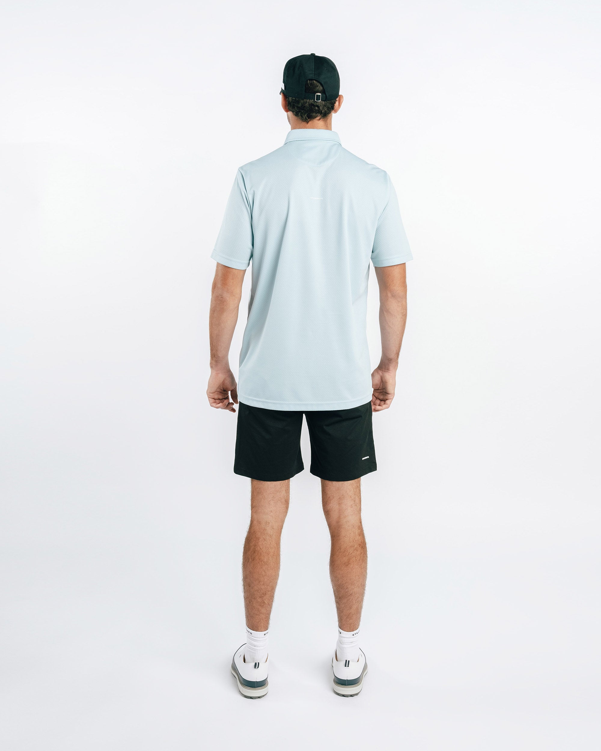 Man wearing a light blue polo shirt and black shorts on a white background