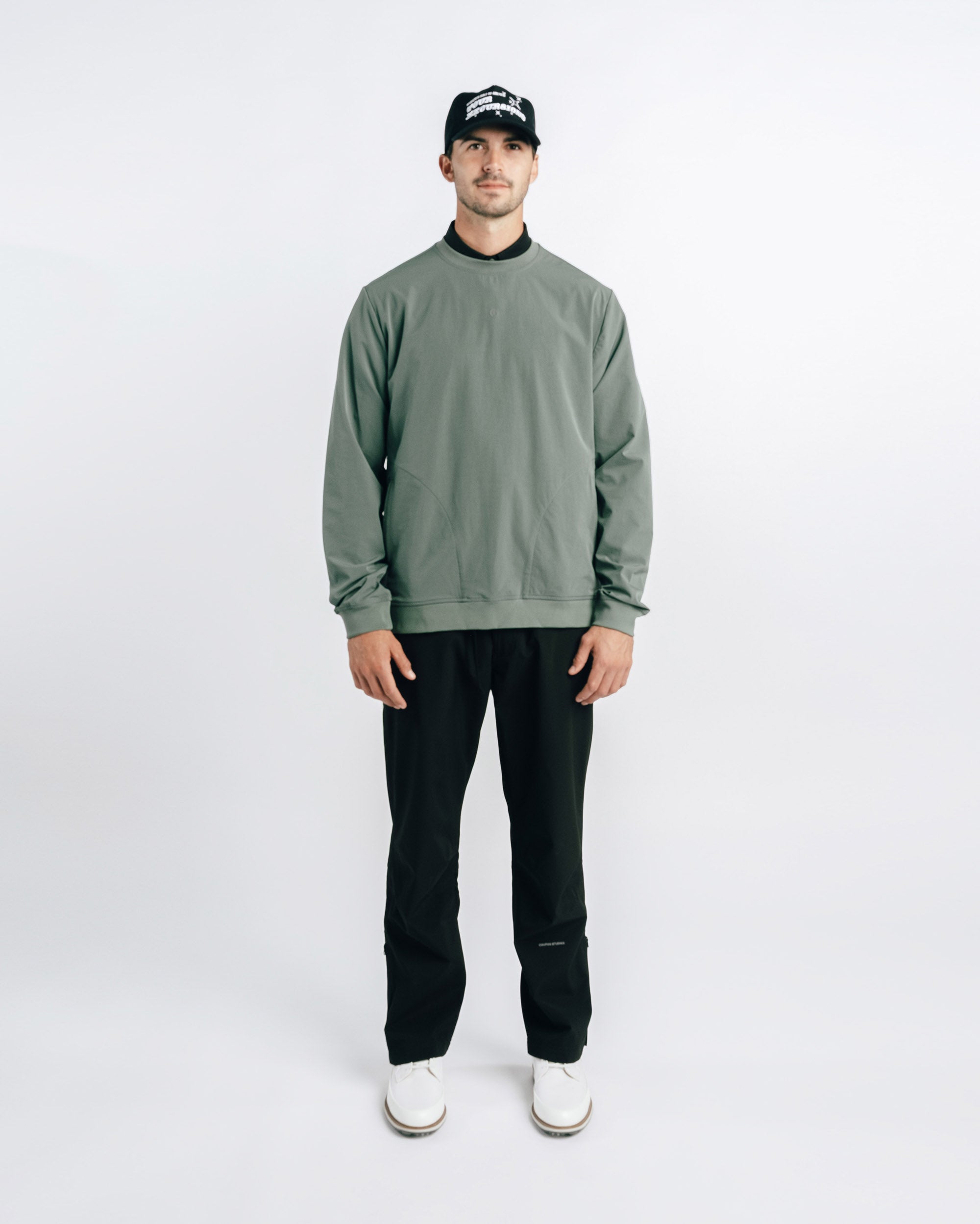 Man wearing a green sweatshirt and black pants on a white background