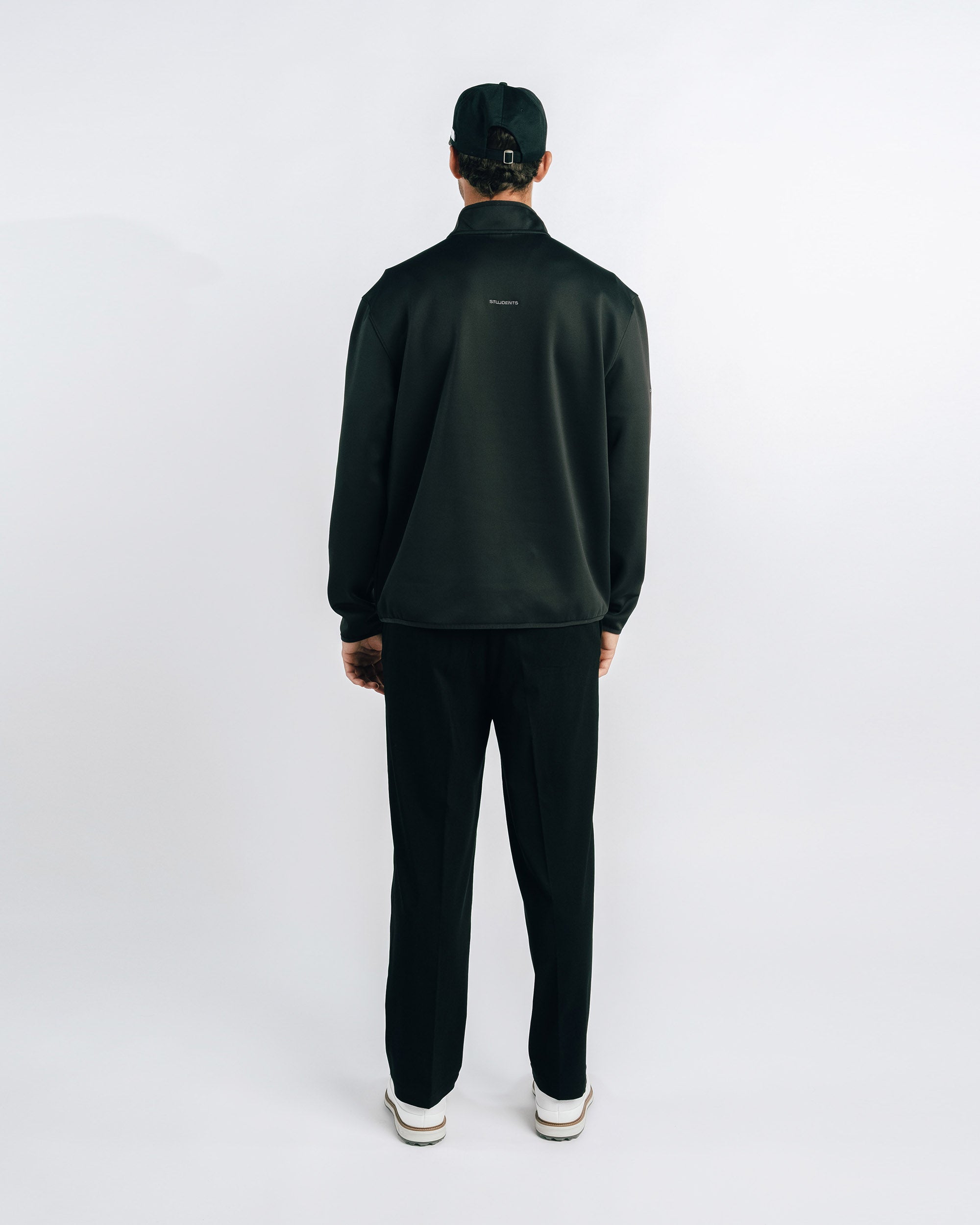 Person wearing a black tracksuit and cap on a white background