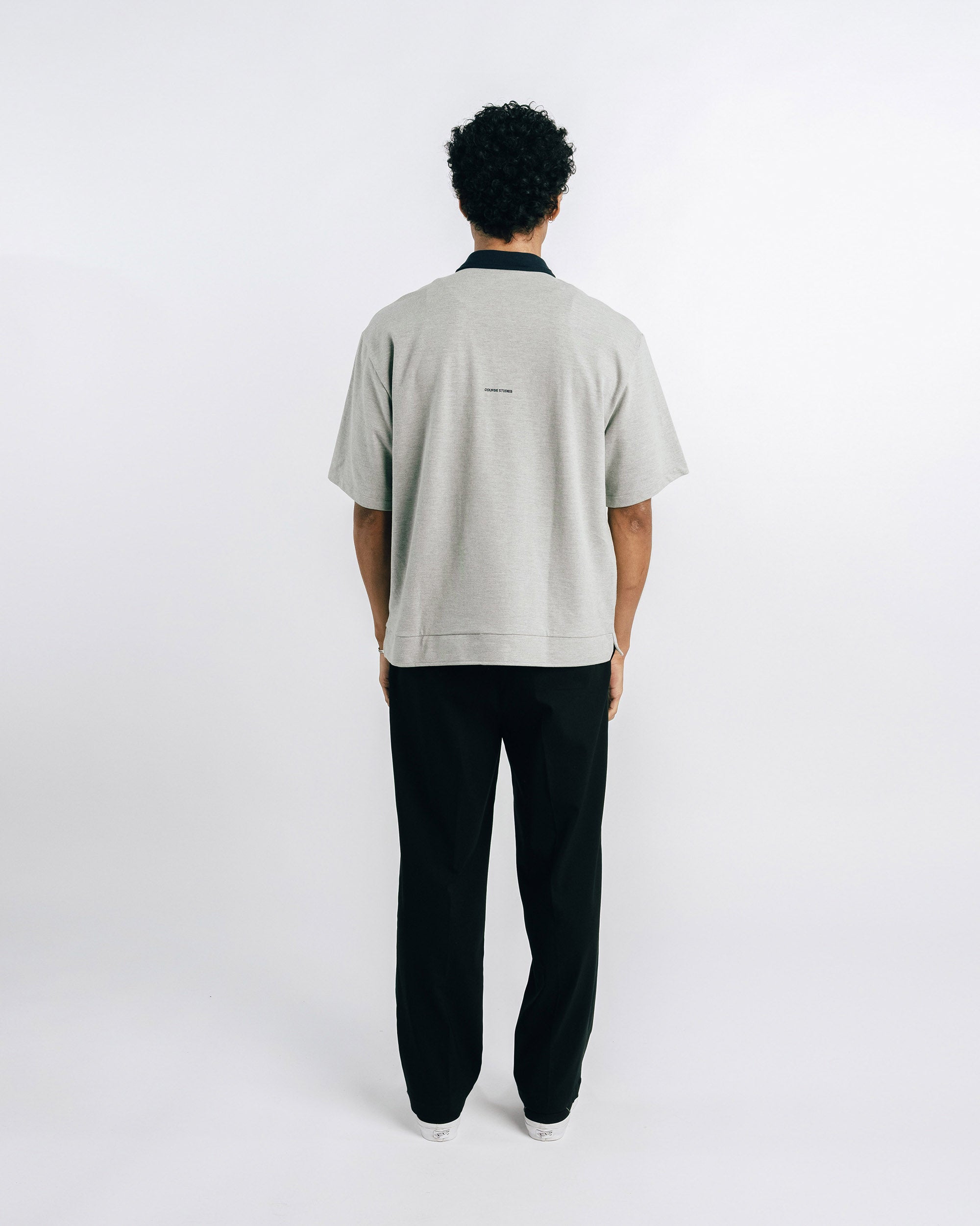 Person wearing a light gray polo shirt with black collar and trim, standing against a white background