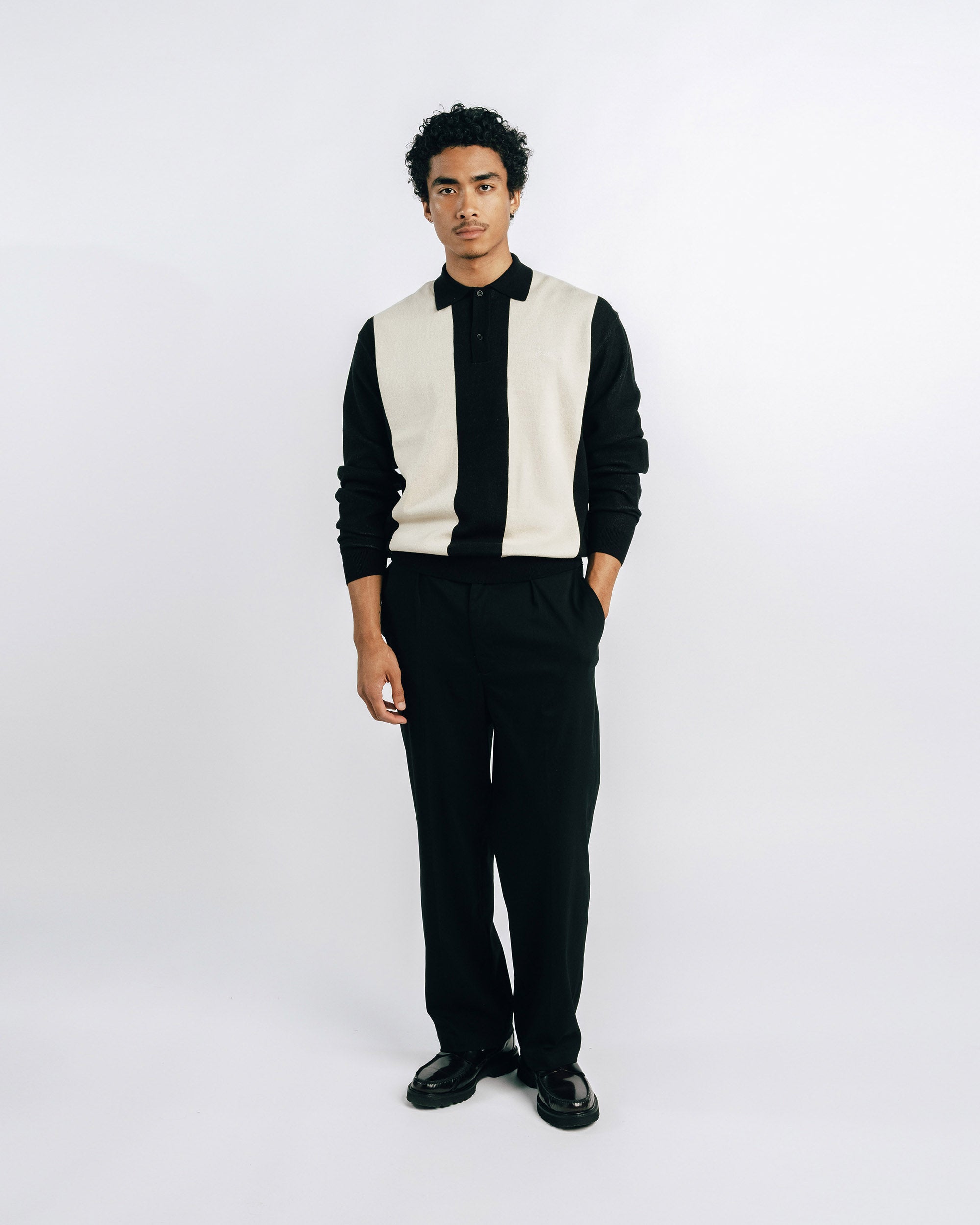 Person wearing a black turtleneck, white vest, and black pants on a white background
