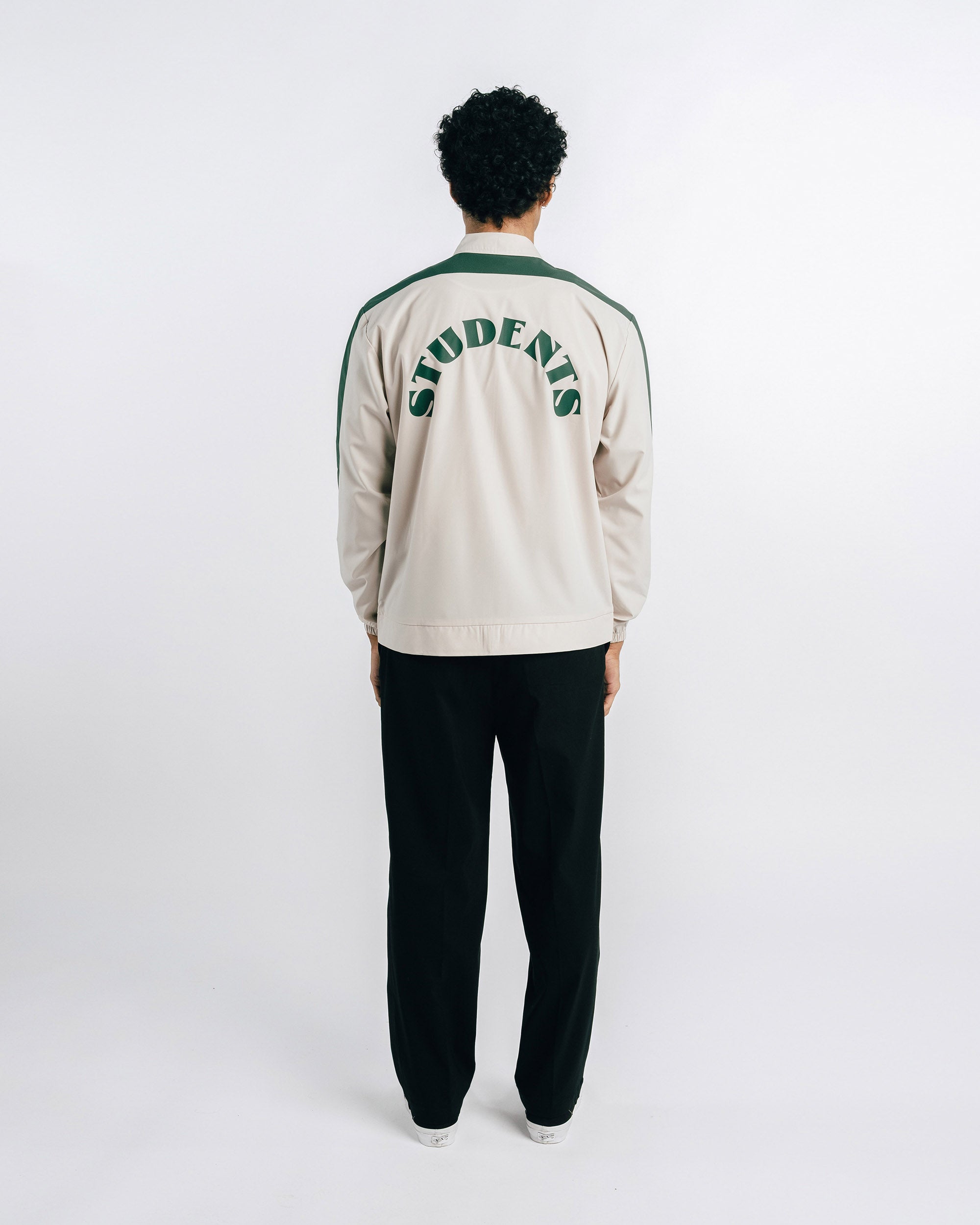 Person wearing a beige tracksuit with 'STUDENTS' text on the back against a white background