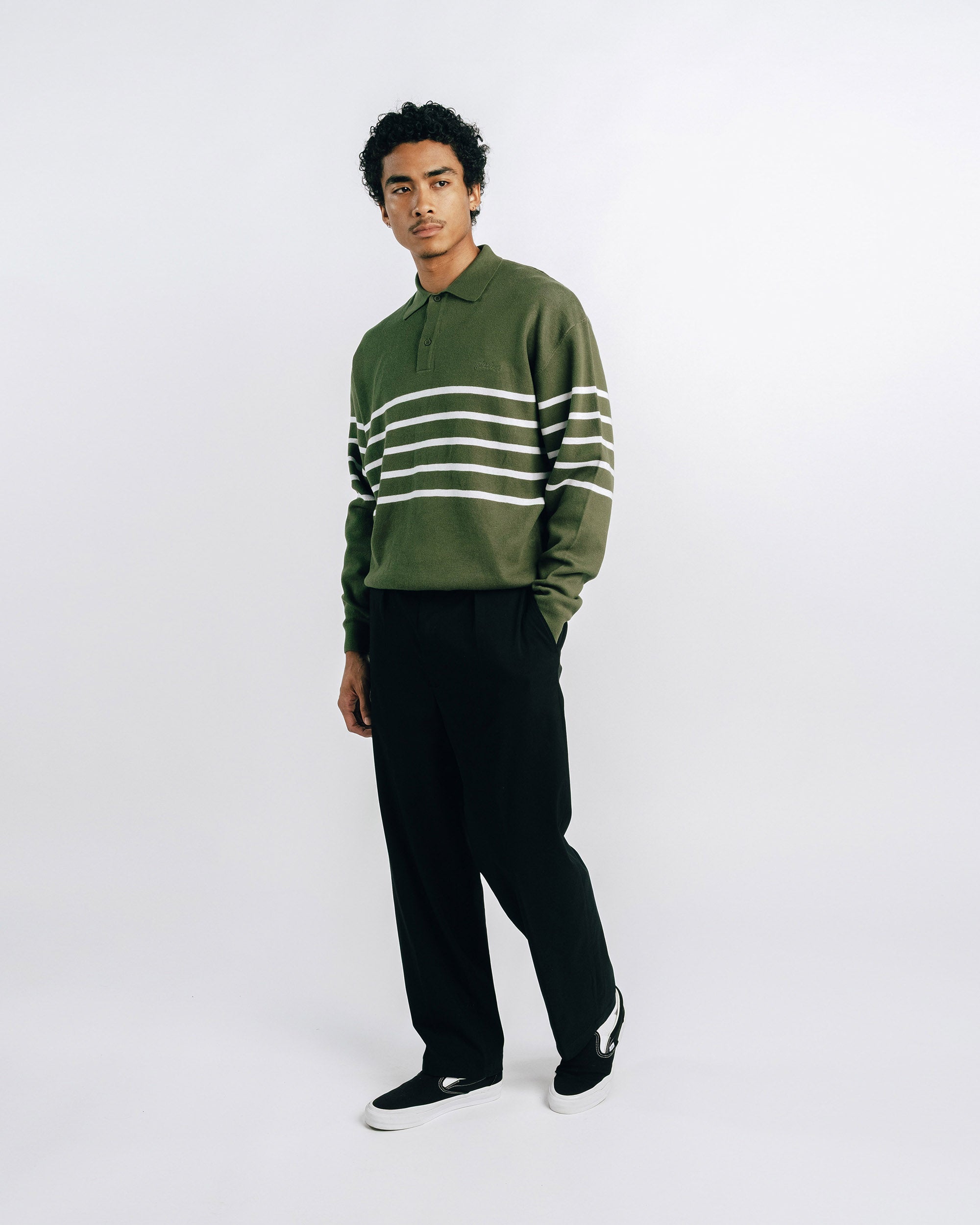 Person wearing a green sweater with white stripes and black pants on a white background