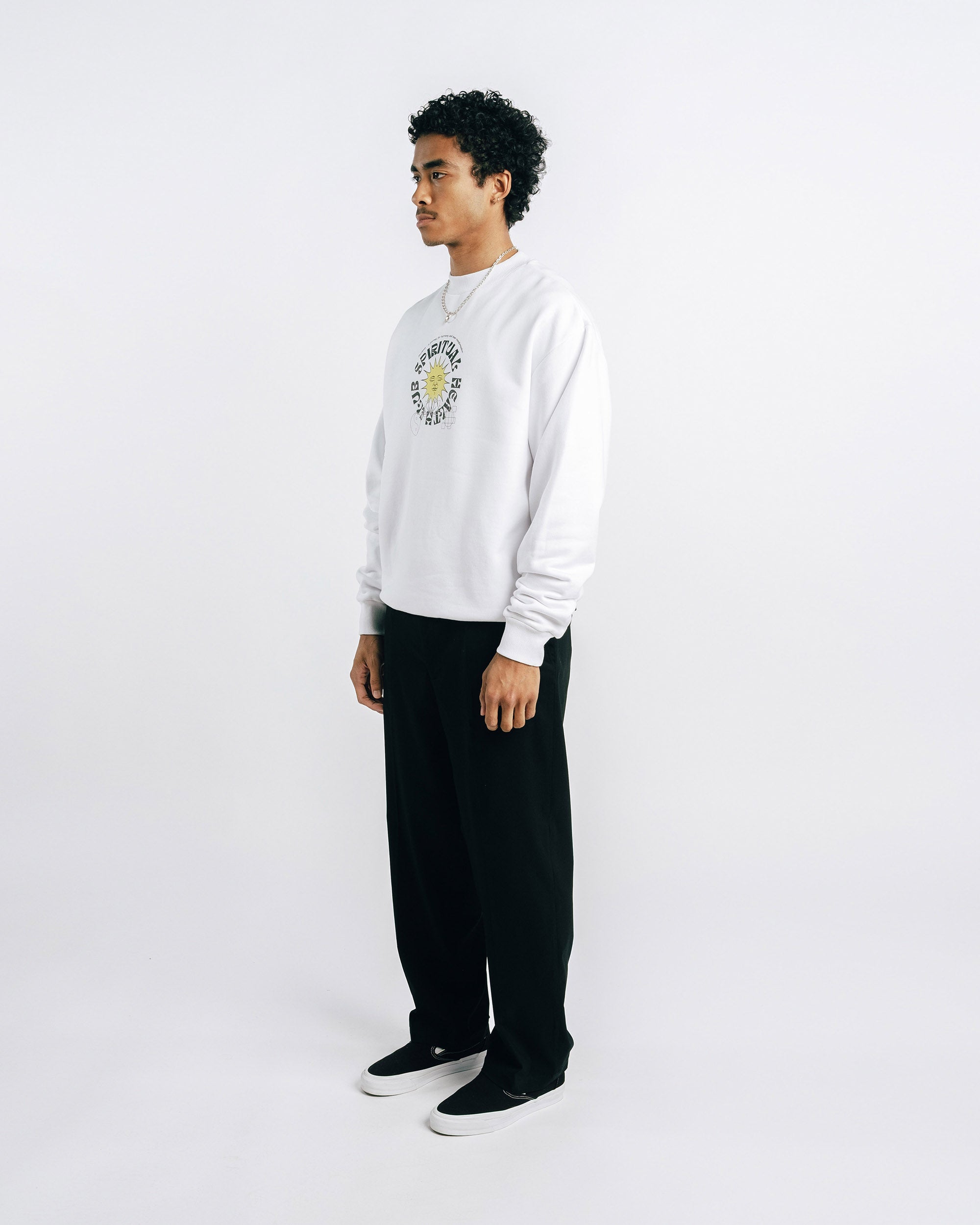 Person wearing a white sweatshirt with a logo and black pants on a white background