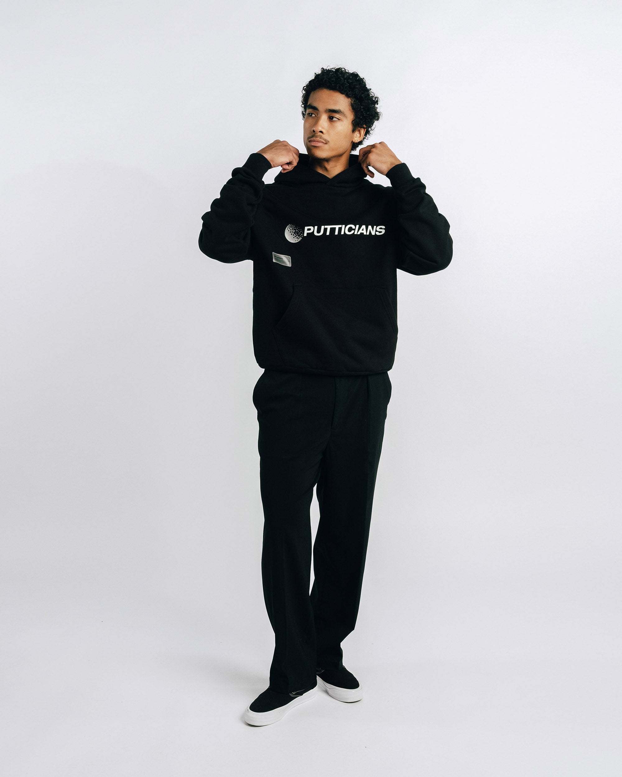 Person wearing a black 'Putticians' sweatshirt and pants on a white background