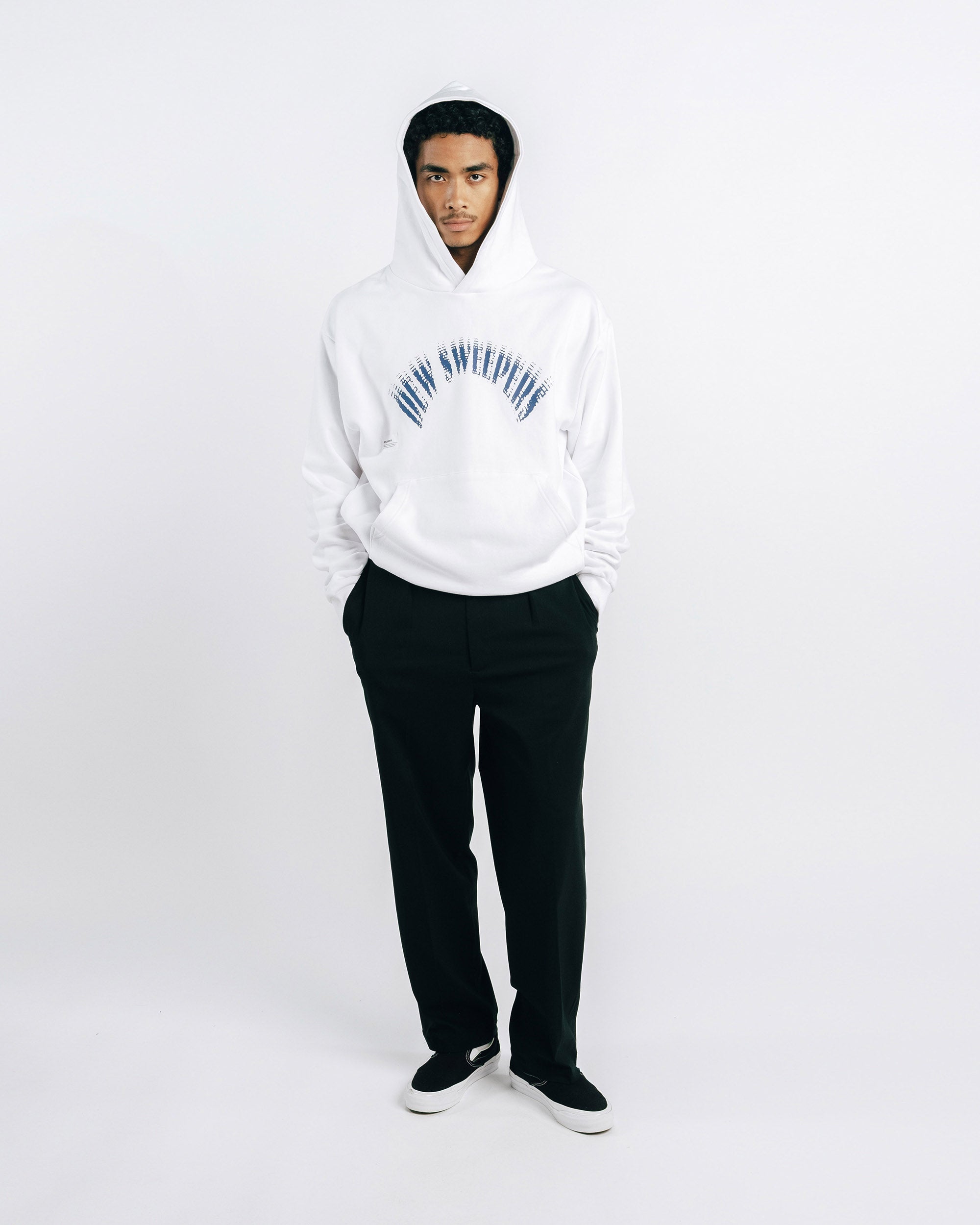 Person wearing a white hoodie with text and black pants on a white background