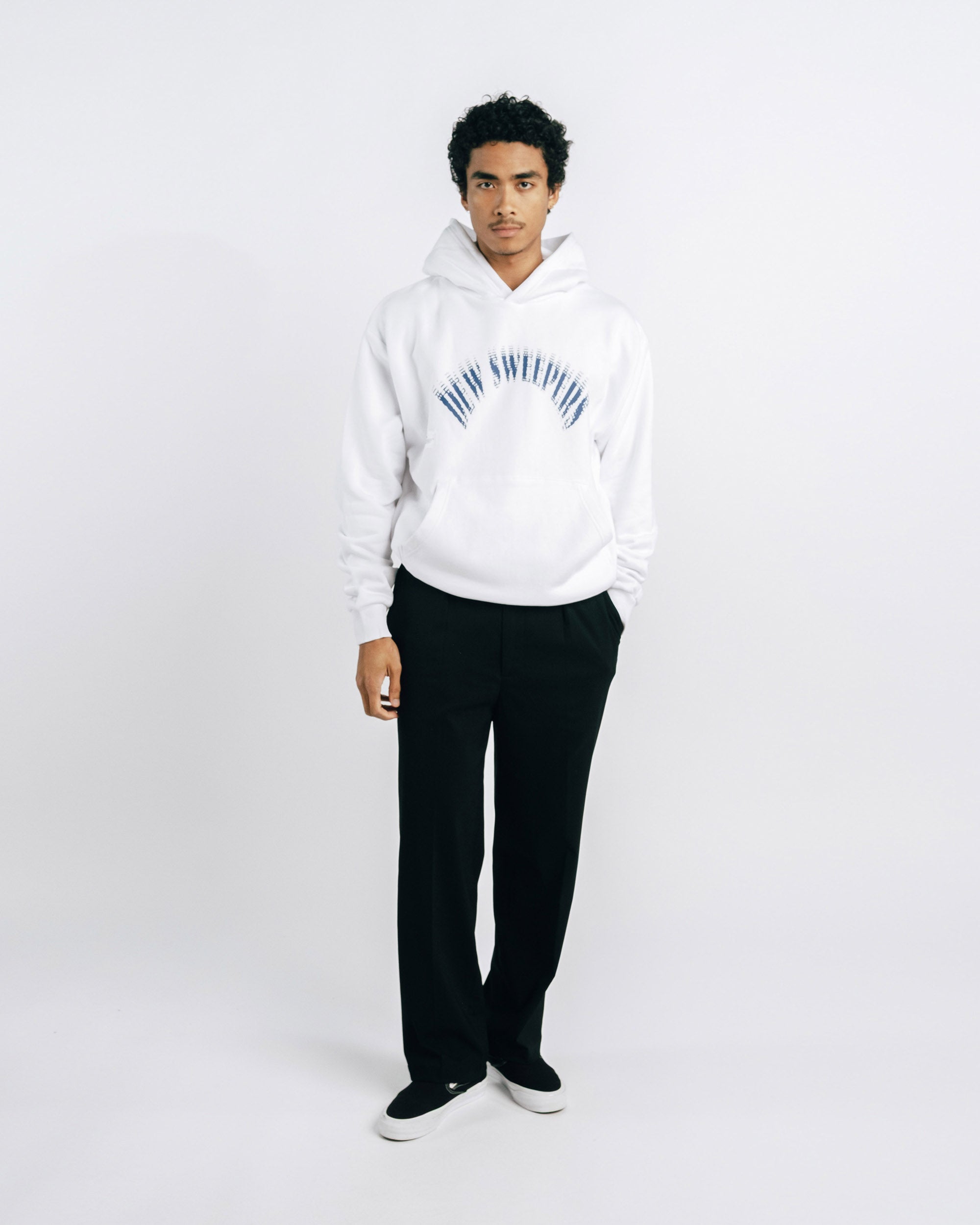 Person wearing a white hoodie with text and black pants on a white background