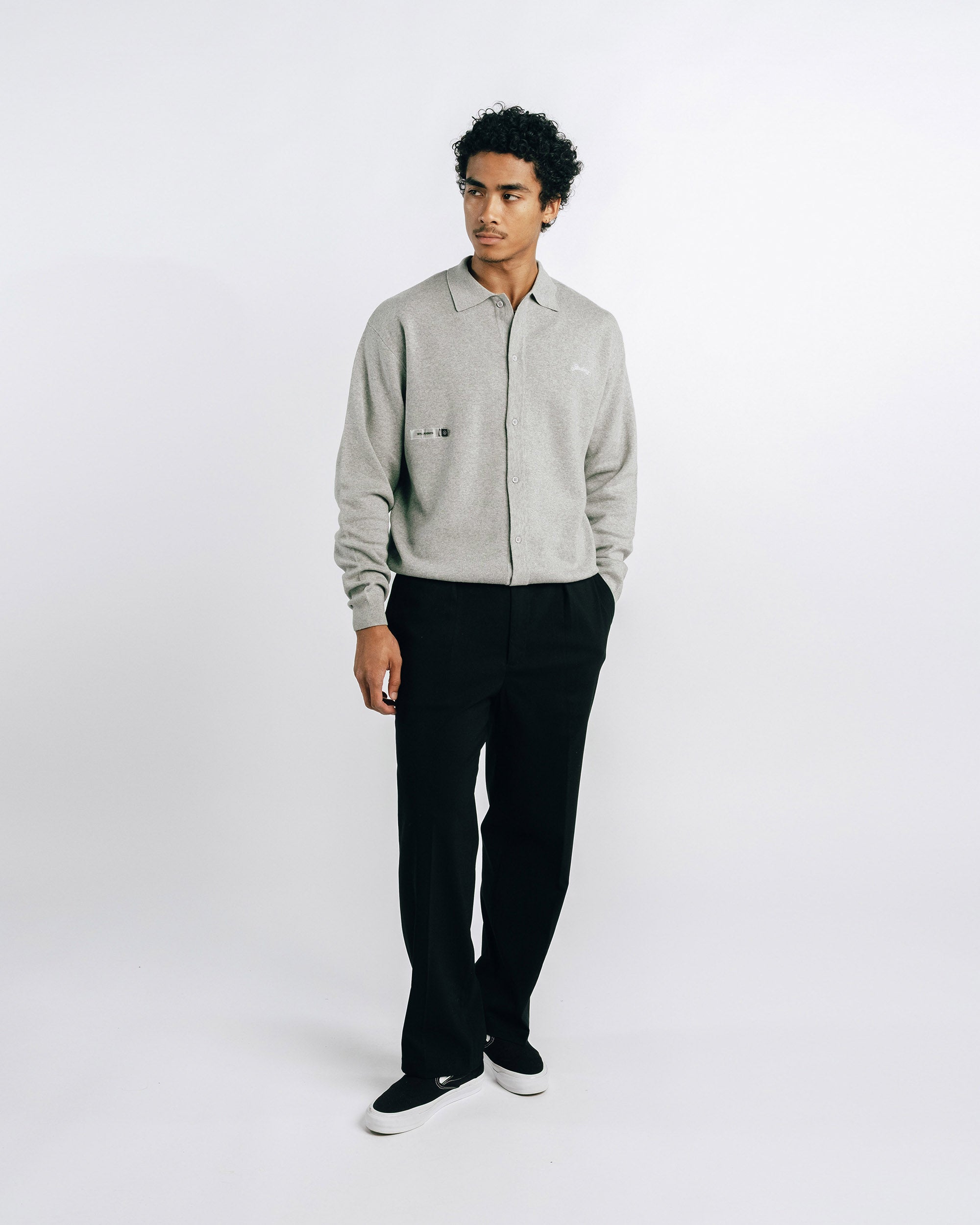 Man wearing a light gray shirt and black pants on a white background