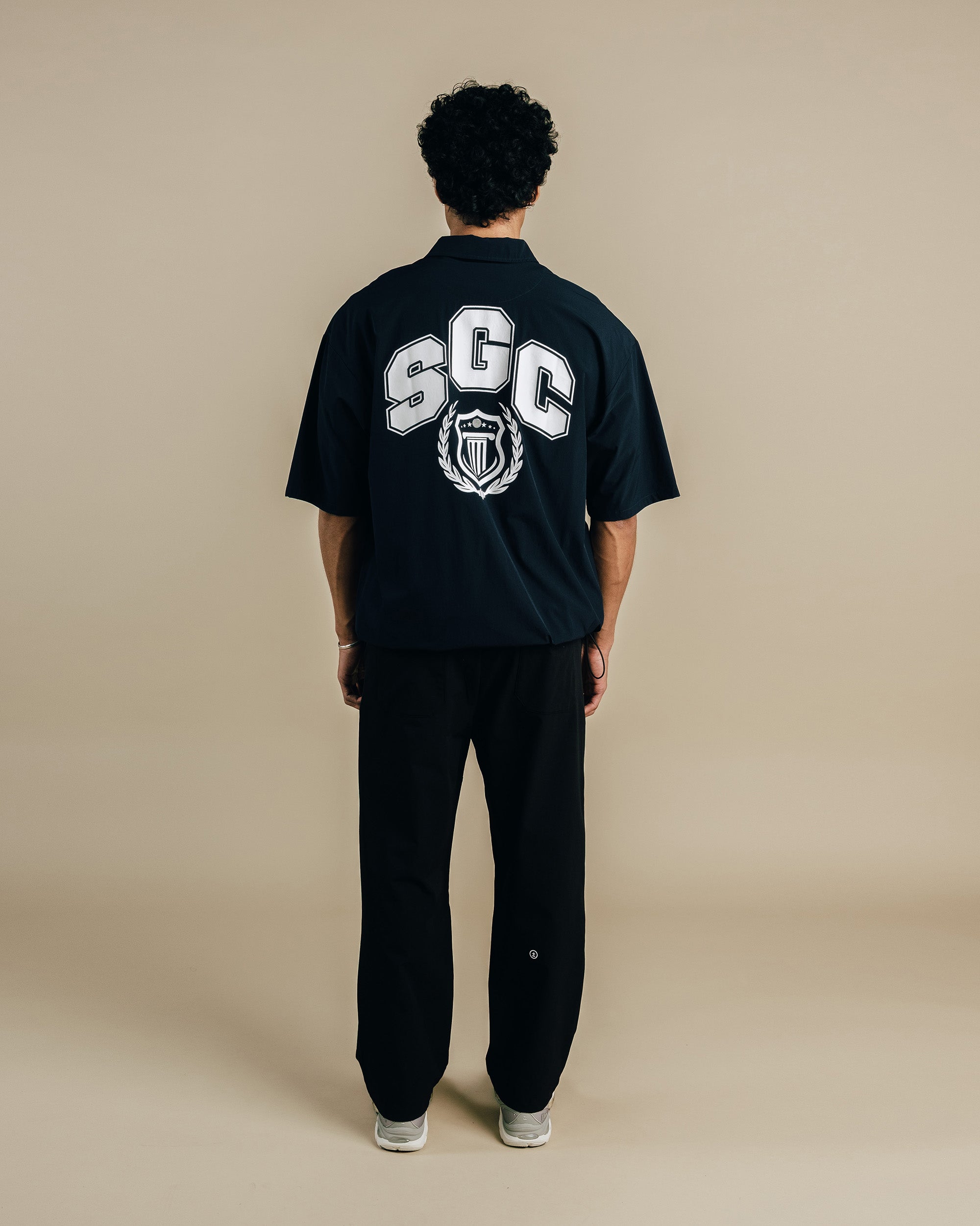 Person wearing a black t-shirt with 'SGC' logo on the back against a beige background