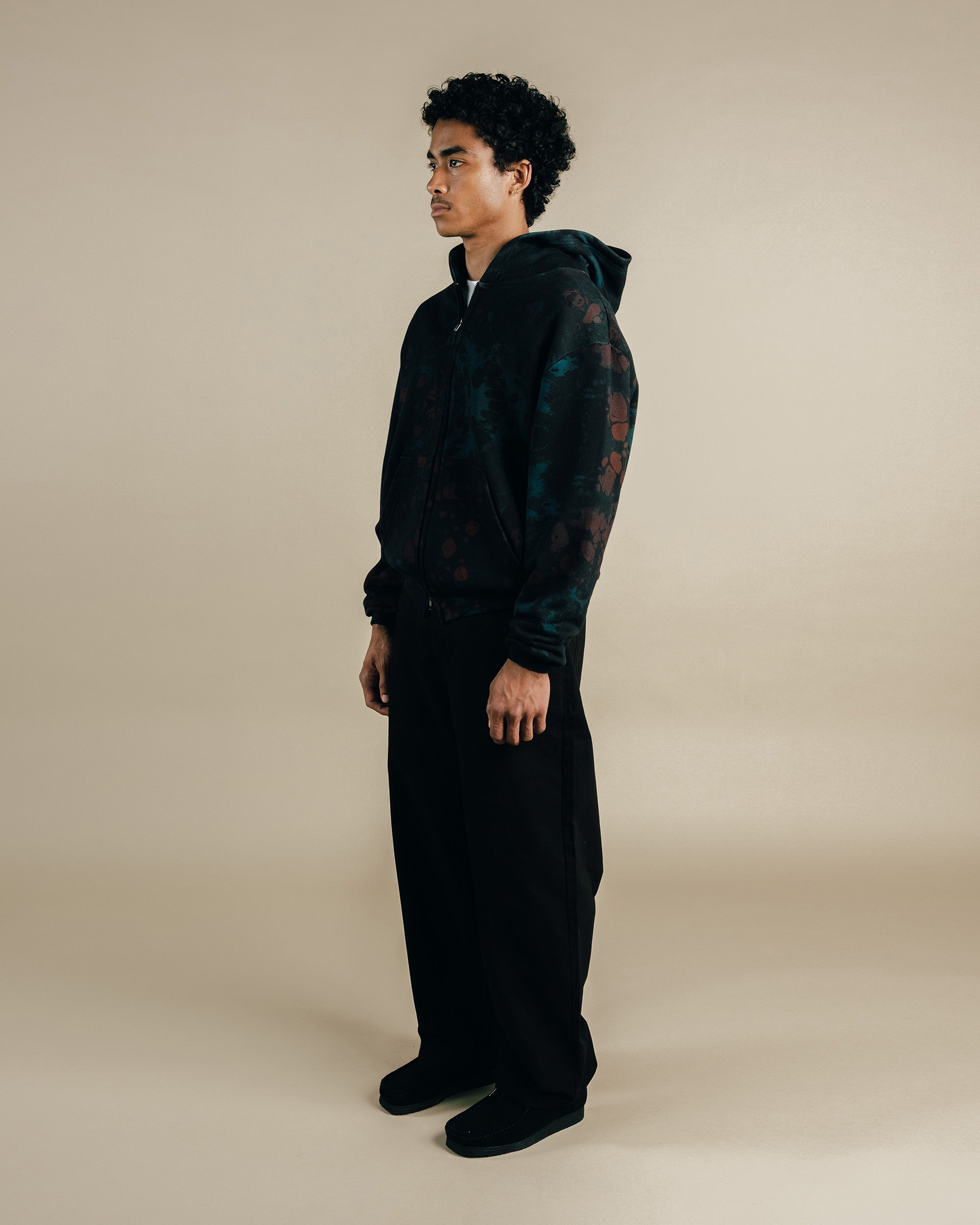 Person wearing a dark hoodie and pants on a beige background