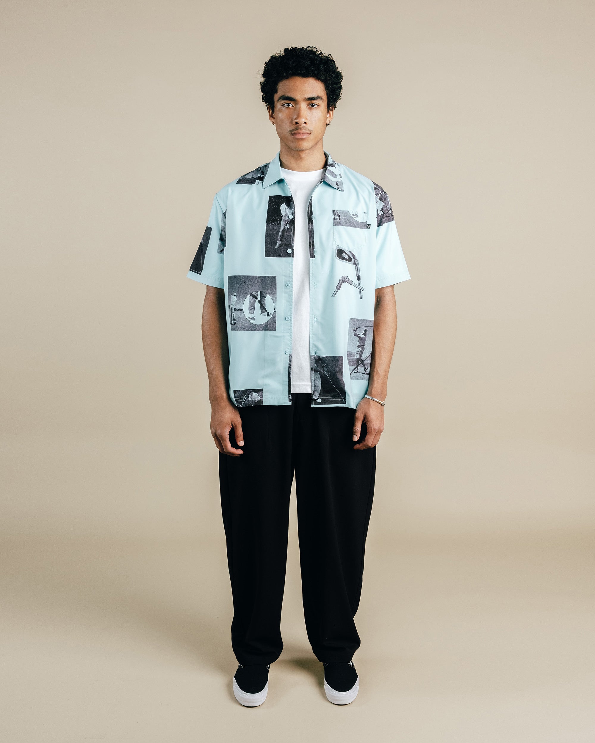 Person wearing a light blue patterned shirt with black pants on a beige background