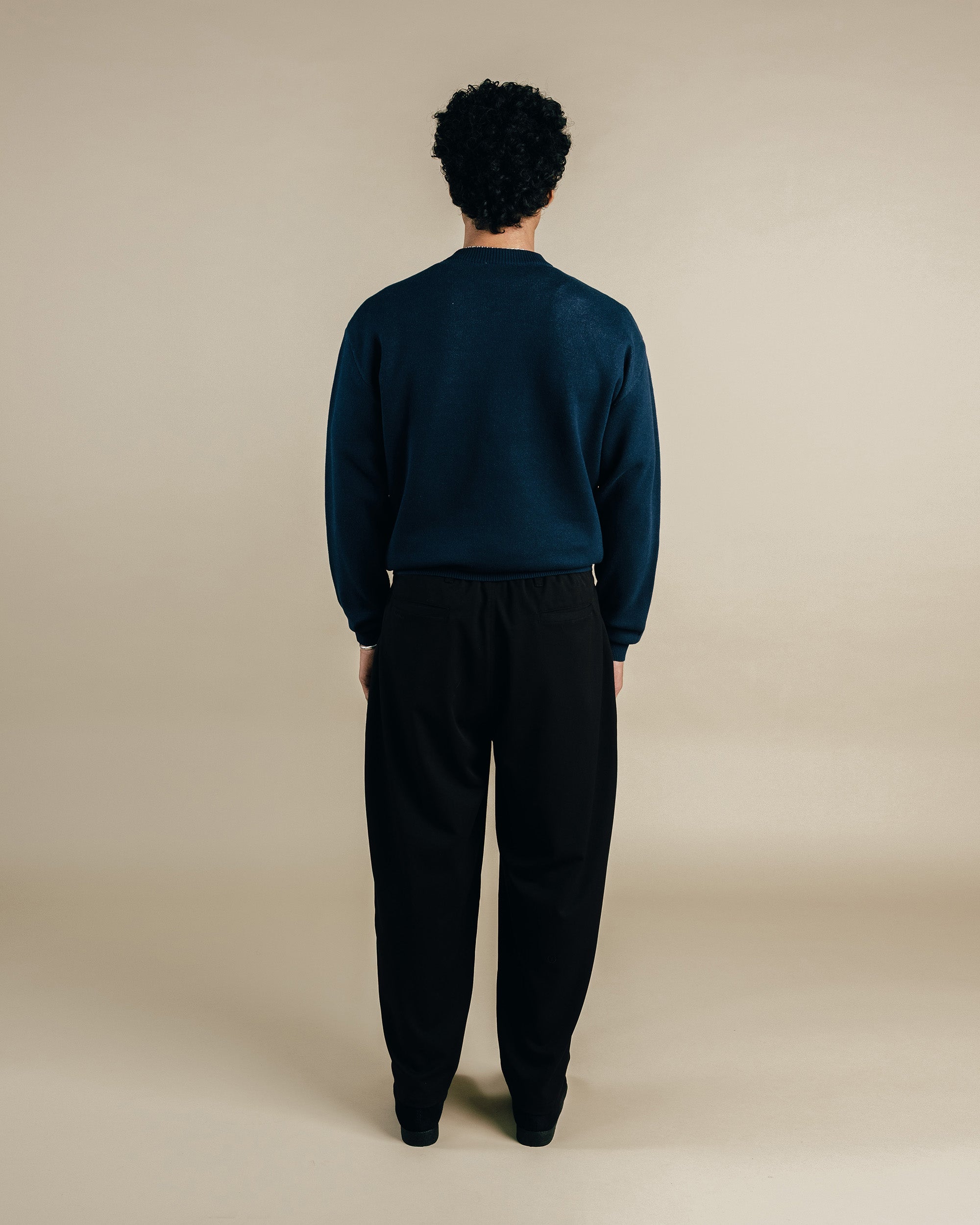 Person wearing a dark green sweater and black pants on a beige background