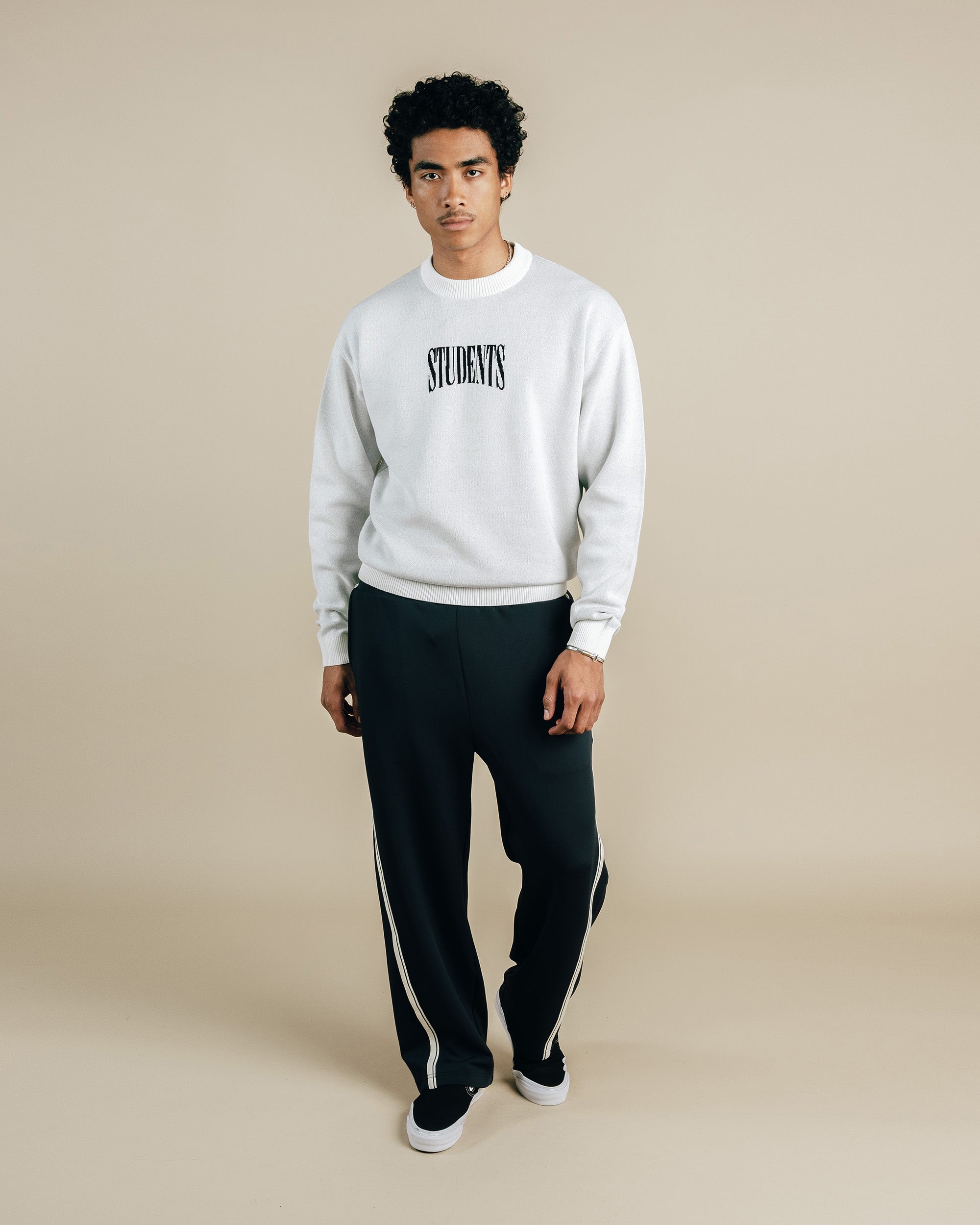 Person wearing a white sweatshirt with 'STUDENTS' text and black pants on a beige background