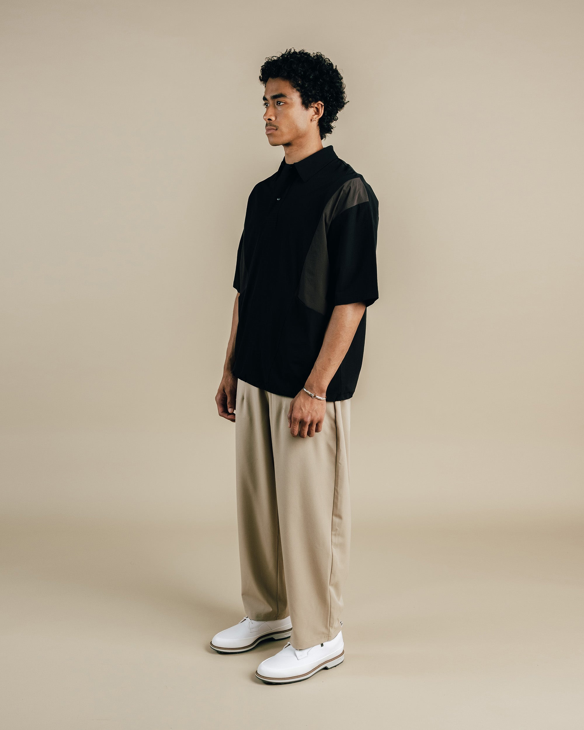 Man wearing a black shirt and beige pants against a beige background
