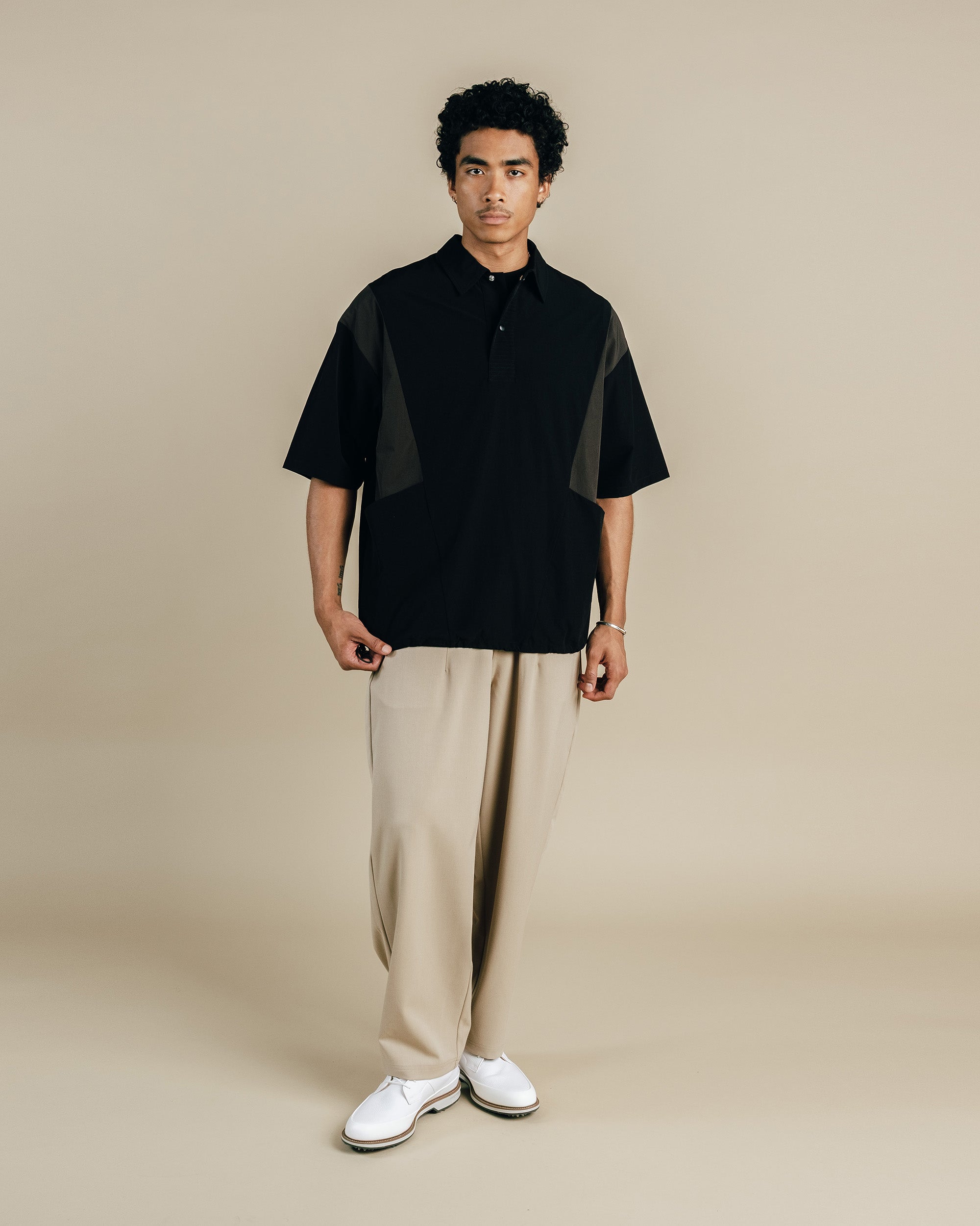 Man wearing a black and gray shirt with beige pants on a beige background