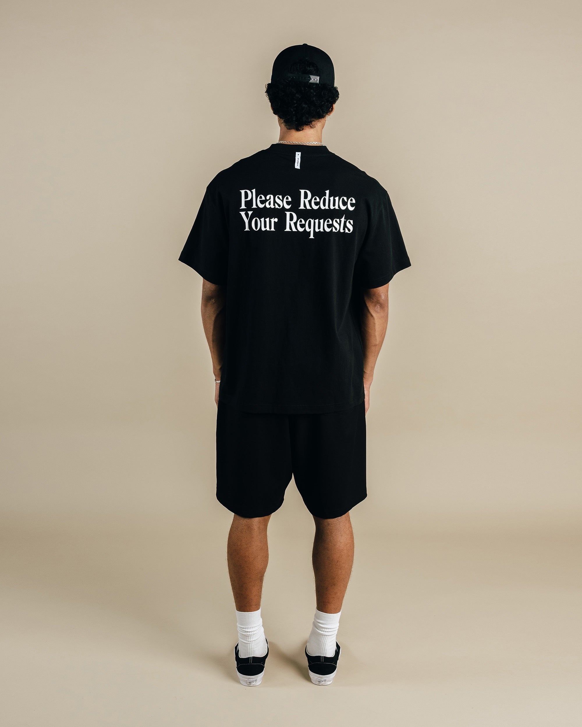 Person wearing a black t-shirt with text on the back against a beige background