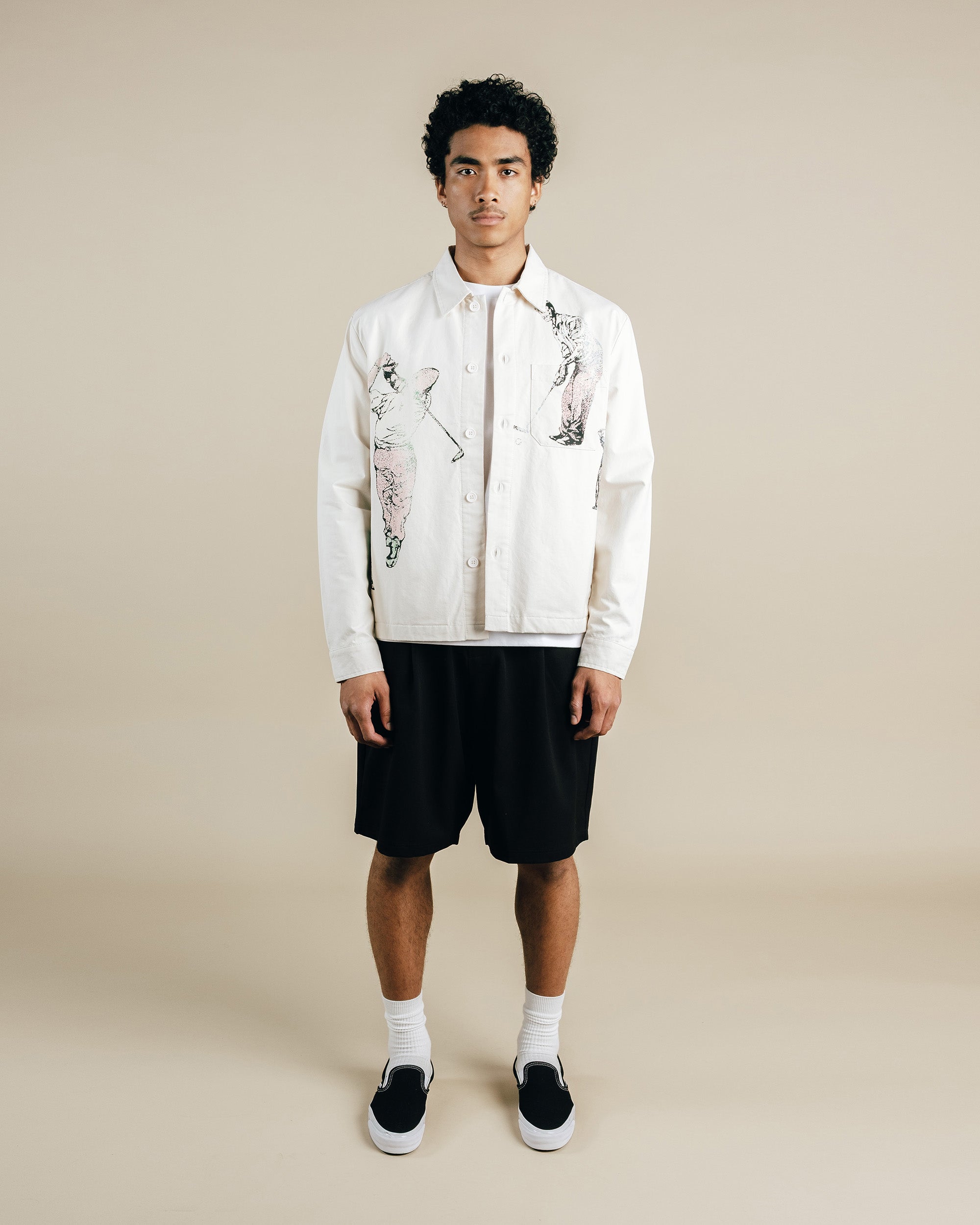 Person wearing a white shirt with graphic designs and black shorts on a beige background