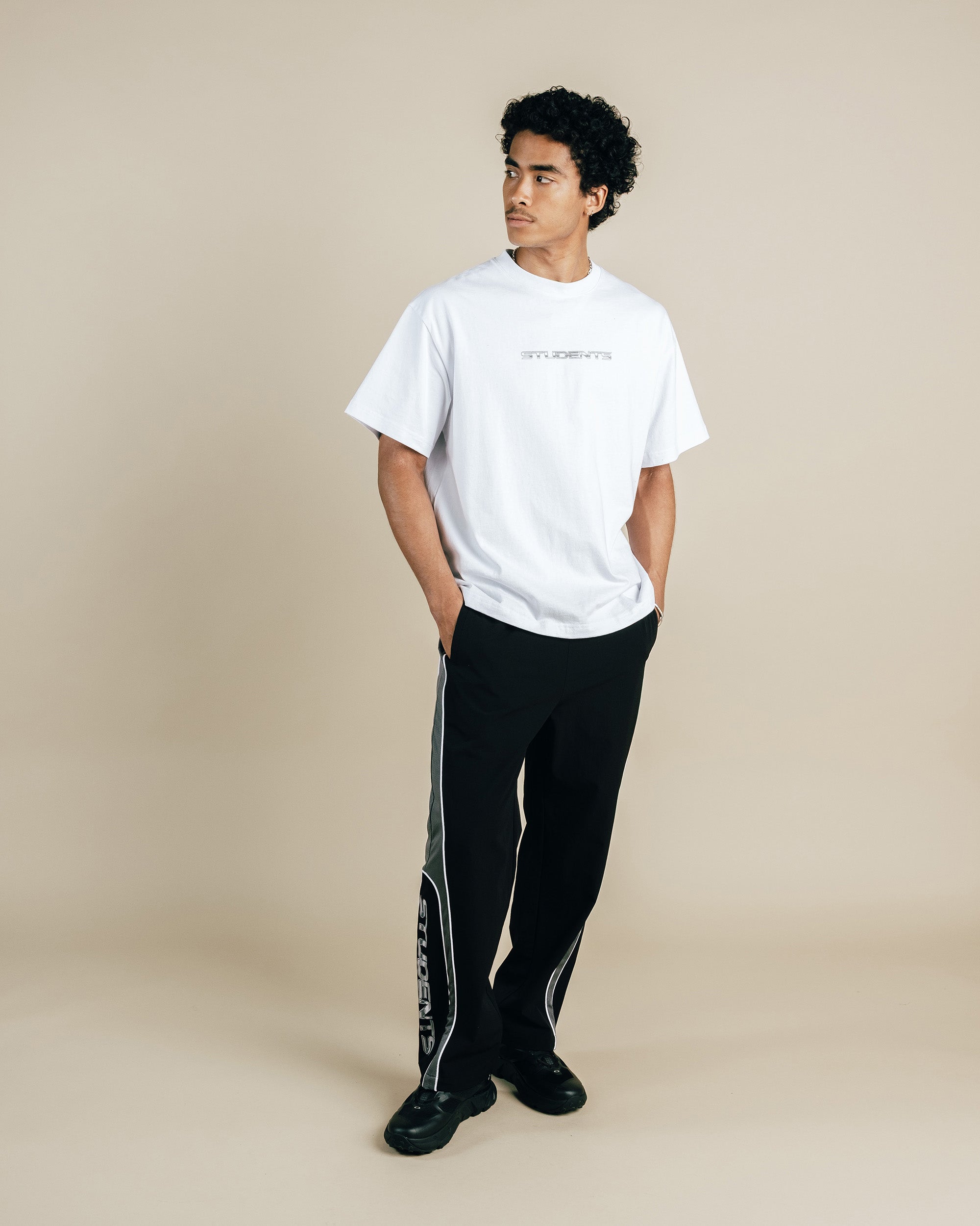 Person wearing a white t-shirt and black pants with a side stripe on a beige background