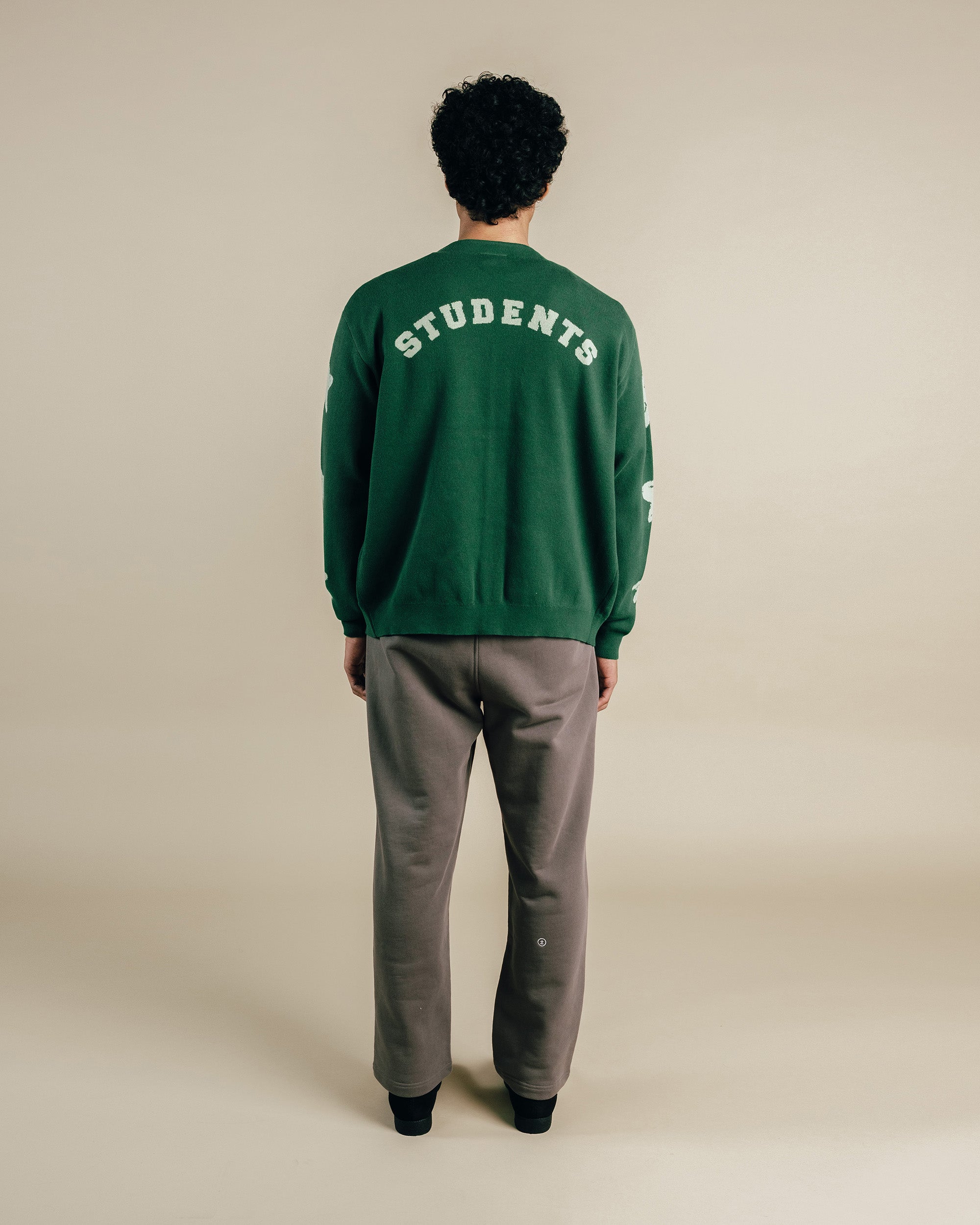 Person wearing a green sweatshirt with 'STUDENTS' text on the back, standing against a beige background.