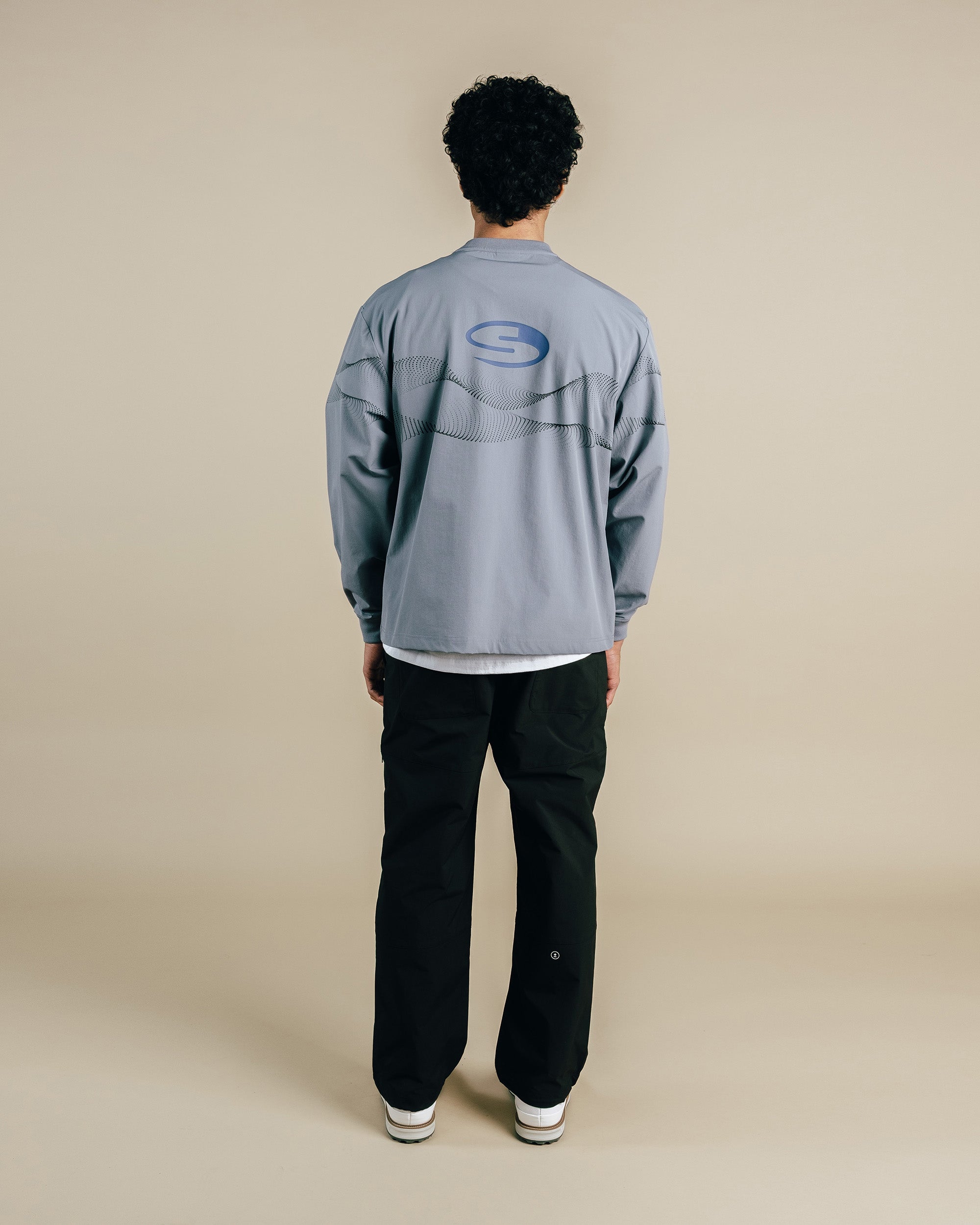 Person wearing a gray long-sleeve shirt with a logo on the back against a beige background