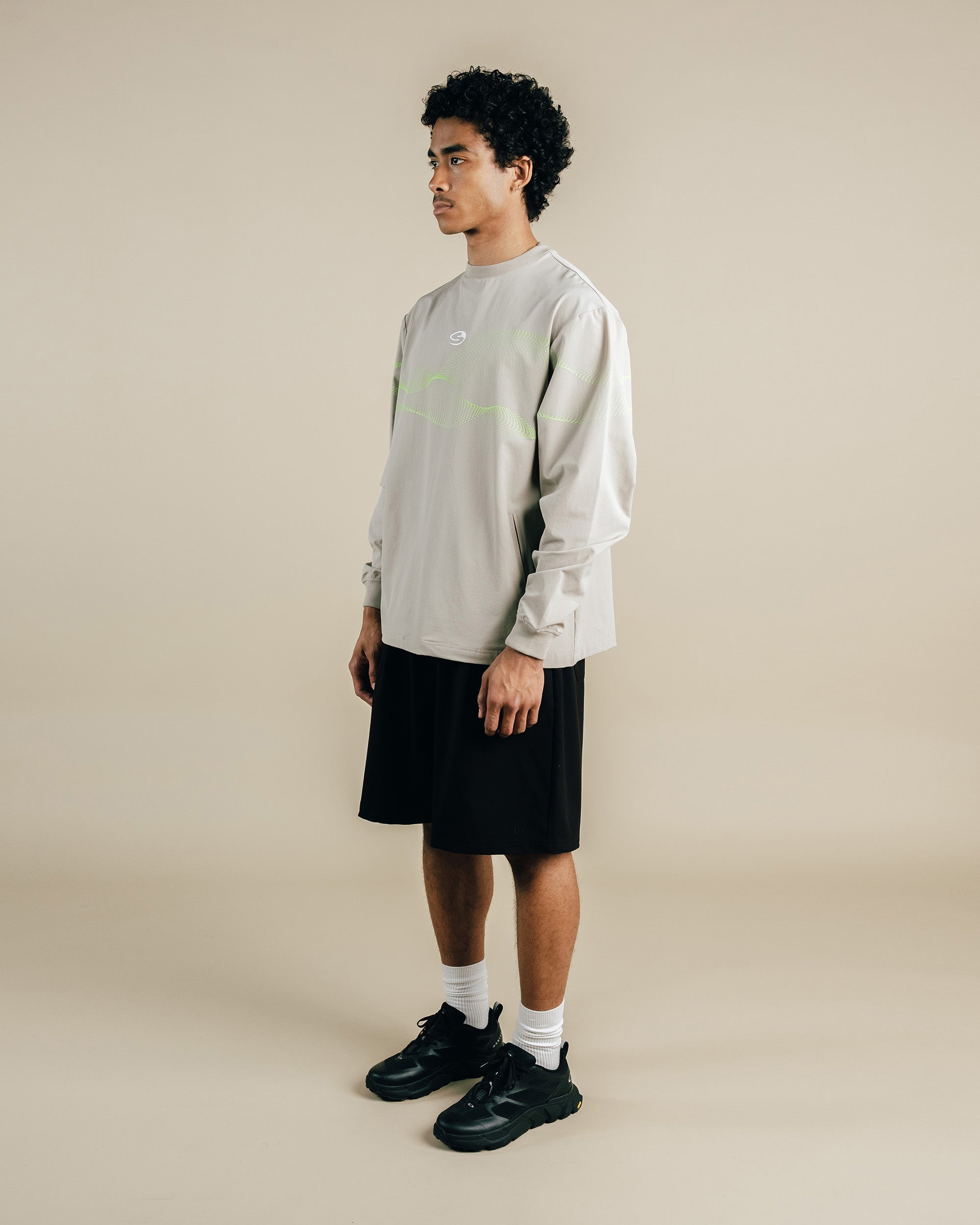 Person wearing a light gray sweatshirt, black shorts, and black shoes on a beige background