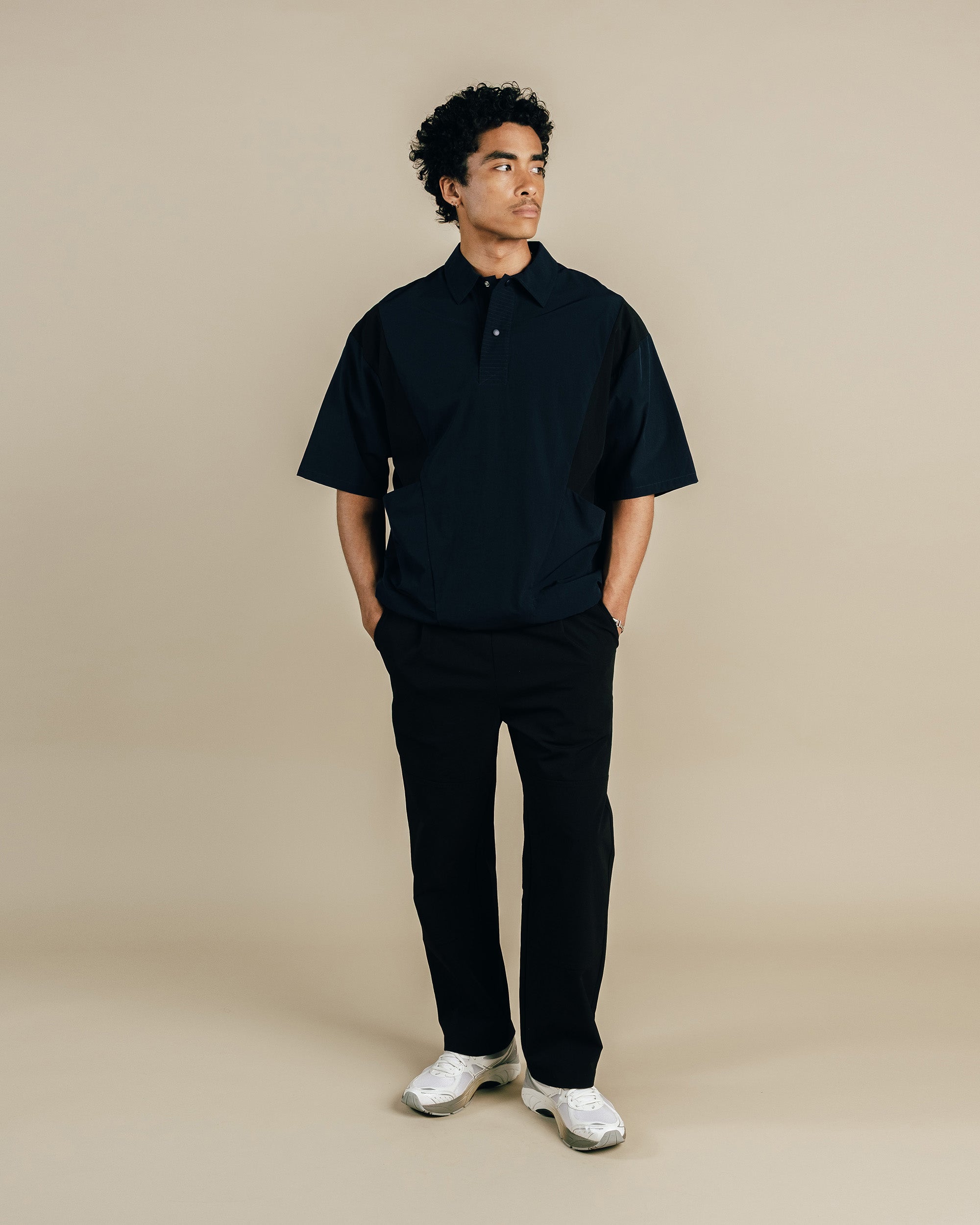 Man wearing a black polo shirt and pants against a beige background