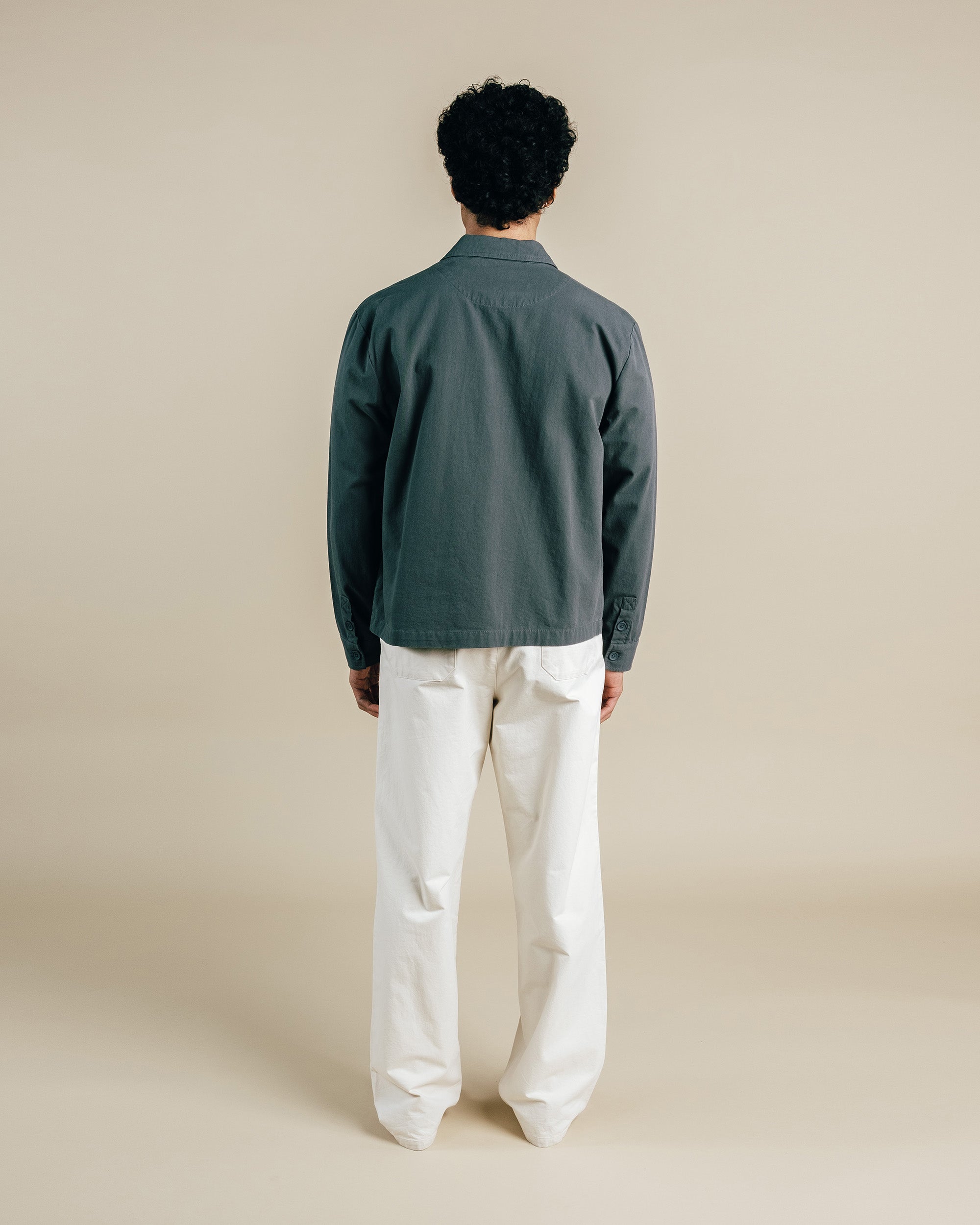 Person wearing a dark green shirt and white pants on a beige background