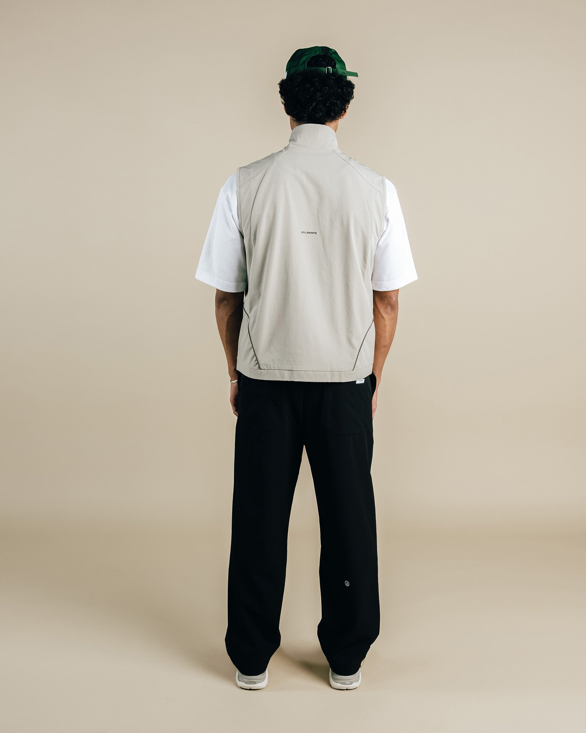 Person wearing a light gray vest over a white shirt with black pants on a beige background