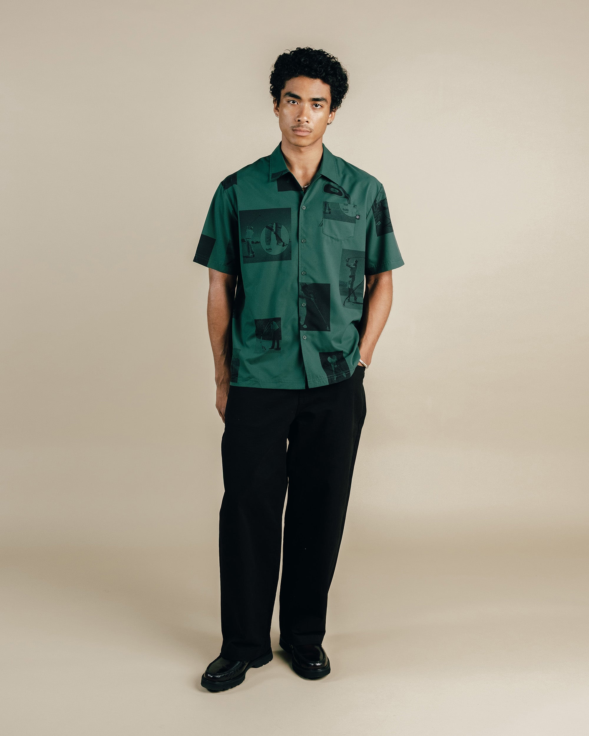 Man wearing a green patterned shirt and black pants on a beige background